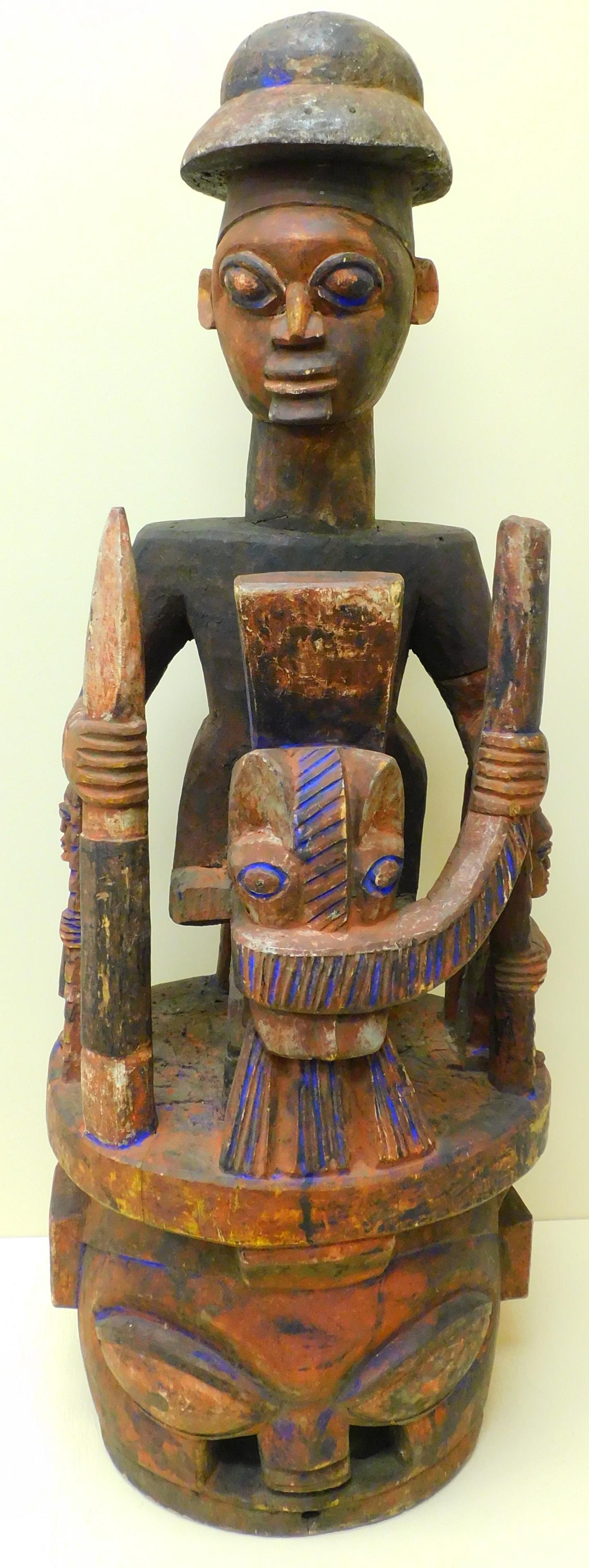 A carved and polychrome painted seated African: warrior figure with spear 20th c, Yoruba people. 42 1/2" high, 14" diameter.