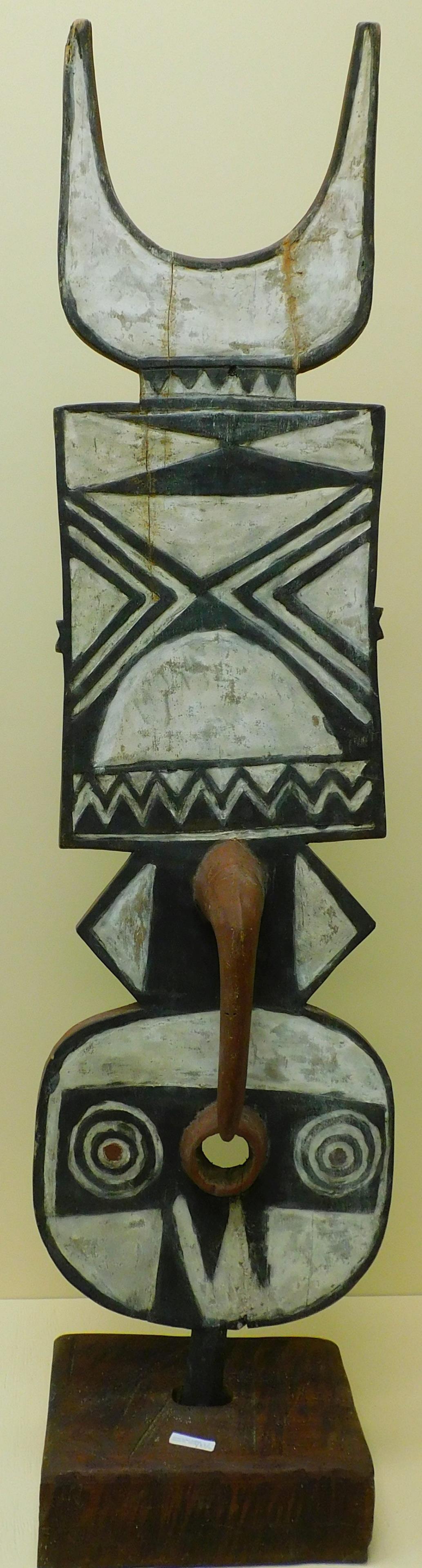 Two 20th century carved and painted African objects.: To include: a carved and painted plank mask with horn, on a wooden base, 59" high, 13" wide. Along with a carved and polychrome decorated headdress, Ambete people, Gabon, 27" high, 5" wide.