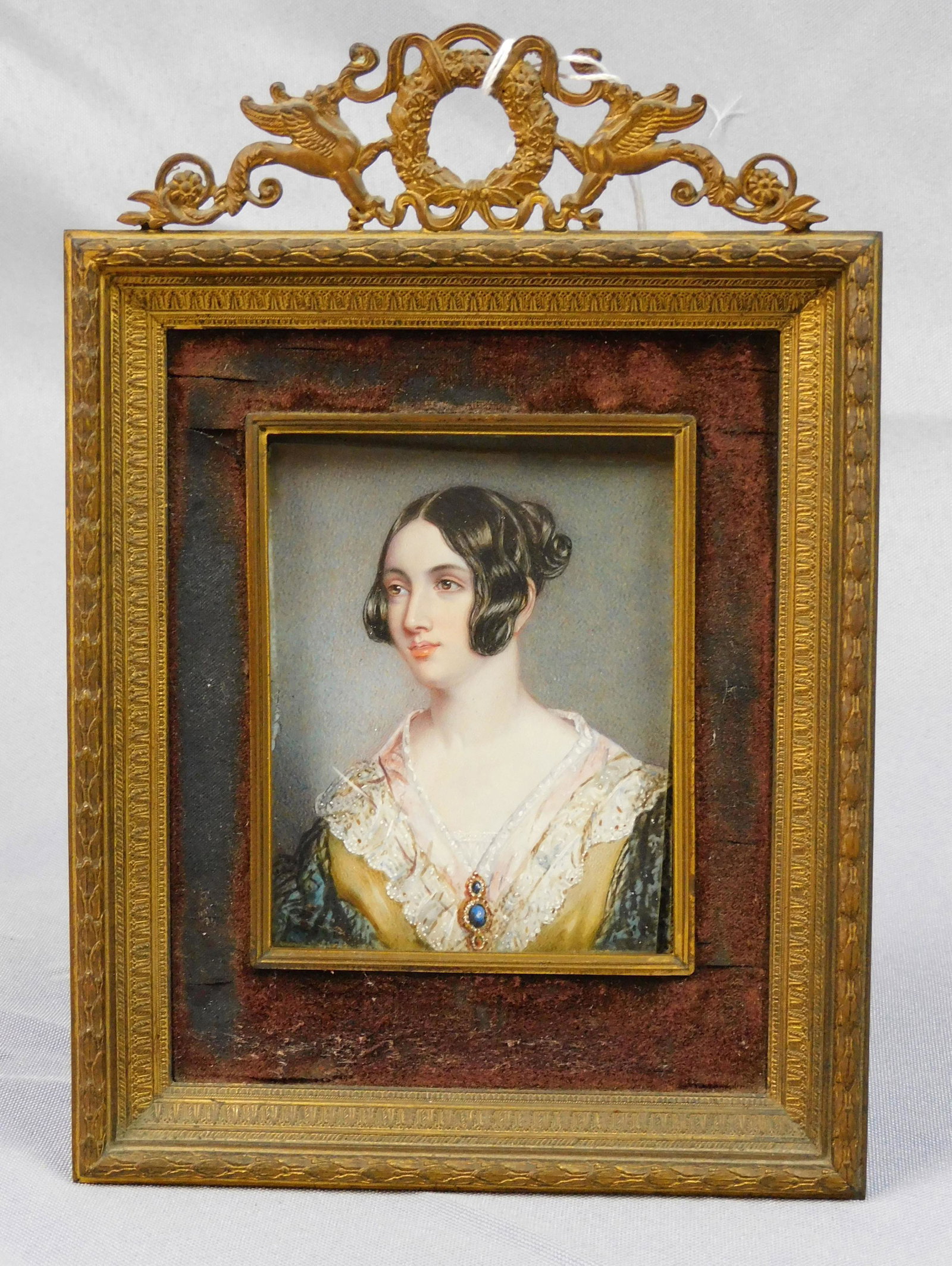 Miniature portrait of an elegantly dressed young: lady, early 19th. In a period brass frame. Sight size 4" x 2 3/4", with frame 8" x 5 1/2". Shows slight paint loss on the left edge, barely visible. Glass is somewhat askew. Provenance: Webb estate.