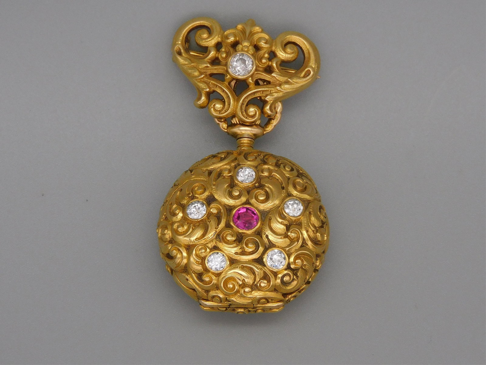 Smith Patterson & Co 18kt gold lady's watch,: early 20th c., on original gold watch pin. Porcelain enameled face with intricately formed clock hands. Swirling repousse case inset with 5 diamonds and one central ruby. The pin from which the watch 