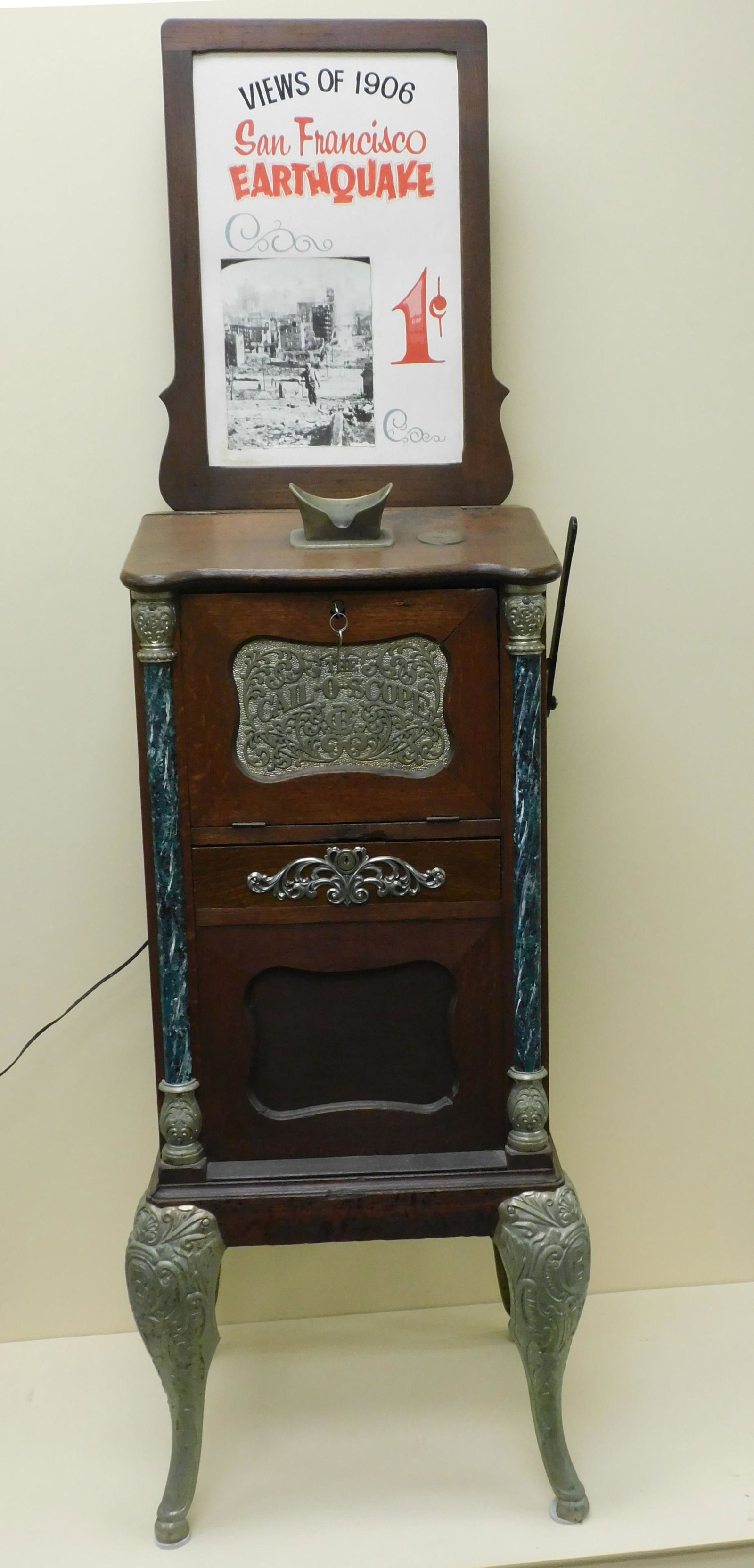 Cail-o-scope 1 cent viewer machine highlighting: images of the 1906 San Francisco earthquake. Early 20th c. Original lithographed advertising panel. Oak case with paneled sides and front. Marbleized columns and fancy cast iron trim and legs. Stereov