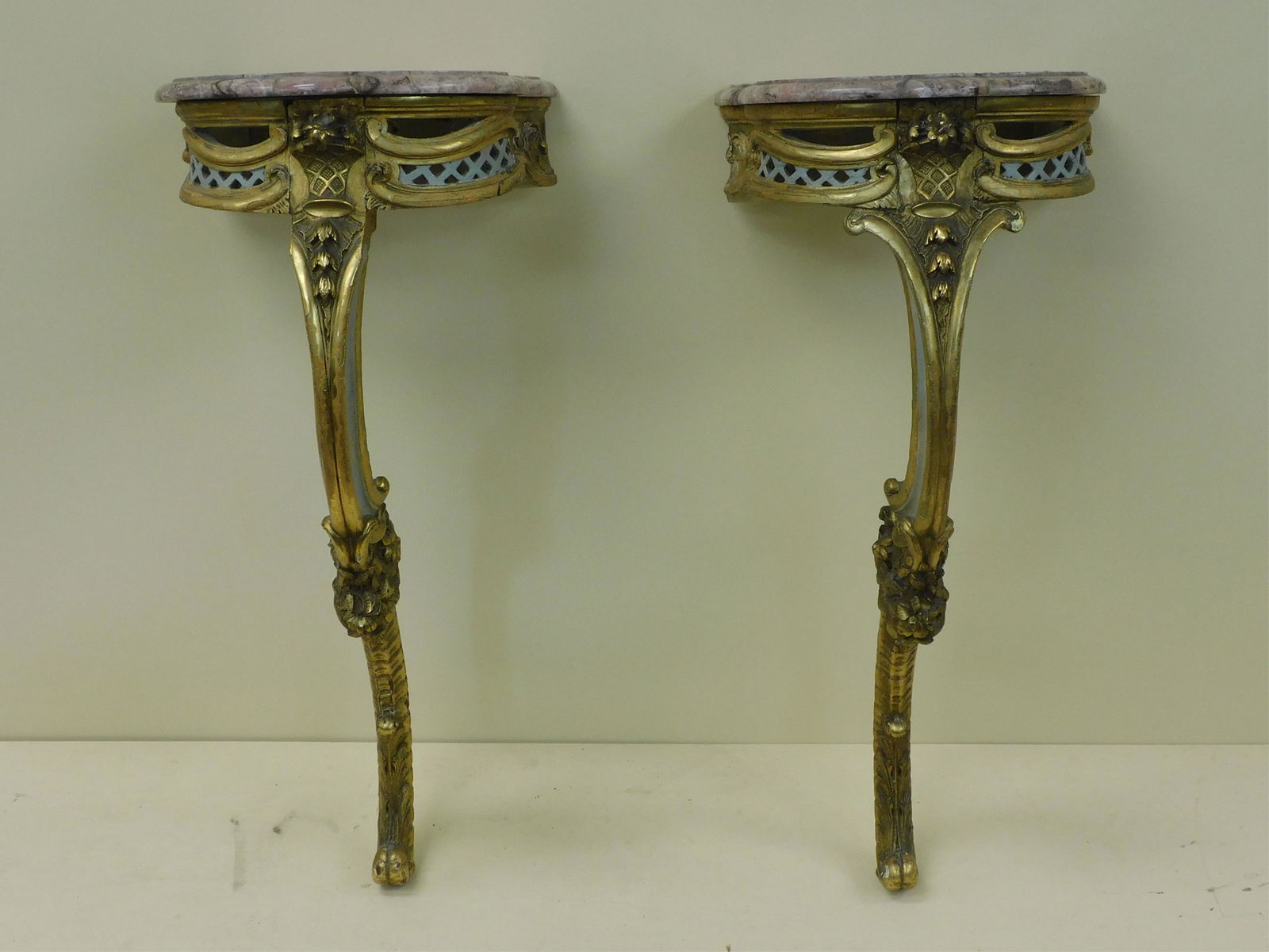 Pair of French console wall mounted stands, 19th: c., Louis XV style. Acanthus leaf and floral, foliate carvings. Gilt wood with white paint accents. Scroll foot. Shaped pink marble tops. Open fretwork to front. One marble shows a missing piece. Both