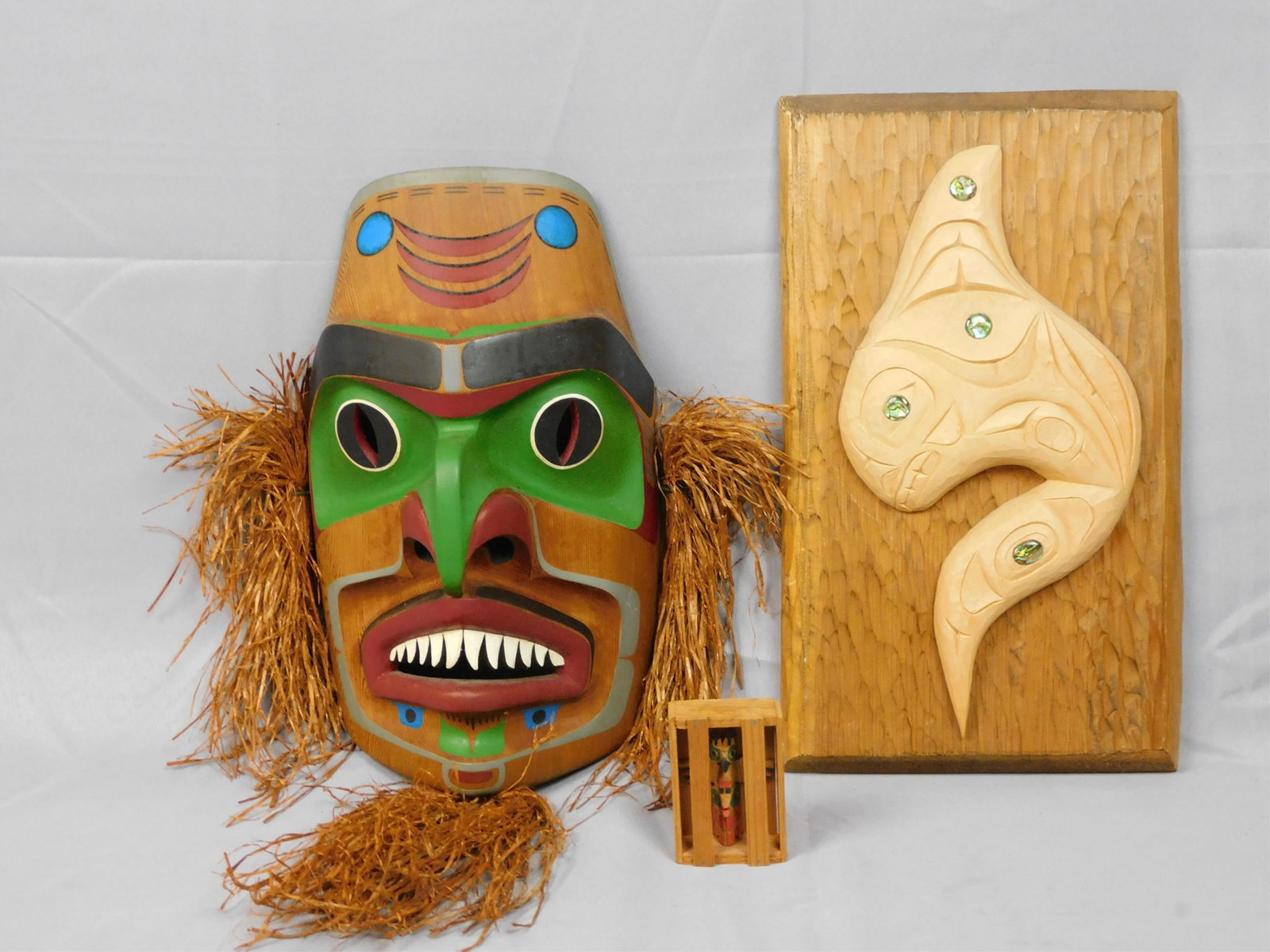 (3) Northwest Coast Carvings. 20th century. Lot: includes a Joe Peters Jr. (1959-1994) Kwa Giulta Shark Mask. Signed and dated 1989. Polychrome painted with fiber ears and beard. 22 overall. Mask 14 1/2" x 8 1/2". Excellent condition. Carved cedar p
