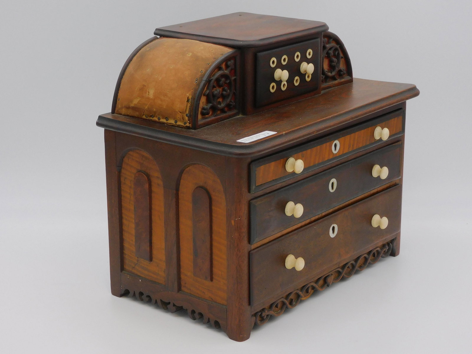 An American miniature sewing stand chest, late: 19th c. The sewing stand is made of walnut and figured maple. The top has double pin cushions and a central spool drawer. The chest features decorative hardware and escutcheons. Shamrock carved motif