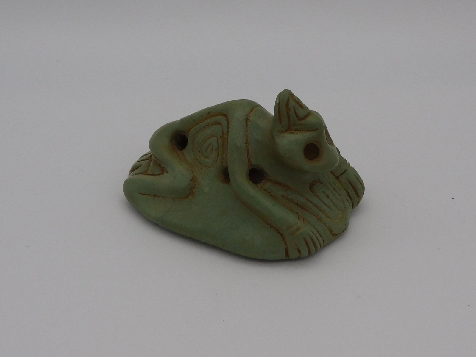 Taino, zoomorphic relief carved figure of a bird.: Head is turned backwards. Pierced at elbows and hips. A water symbol is carved between the ankles at the back of the legs. Base is a group of icons including swirls and wavy lines. Blue gray jasper-li