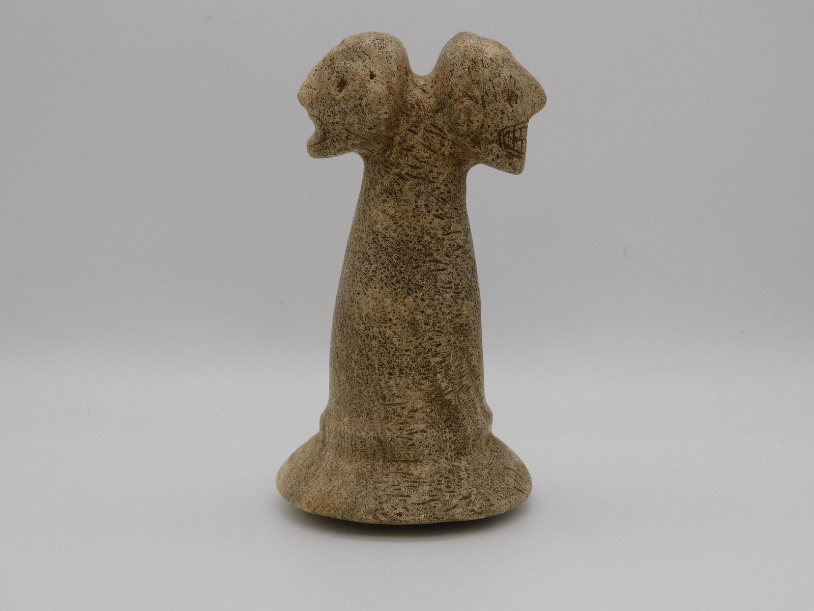 Taino, two headed pestle, one with a closed: mouth, the other with a big toothy smile. Probably used to crush roasted cohoba seeds for hallucinogenic snuffing. The 2 Janus heads represent the Taino belief in duality. Made from fossil coral. 5.8"