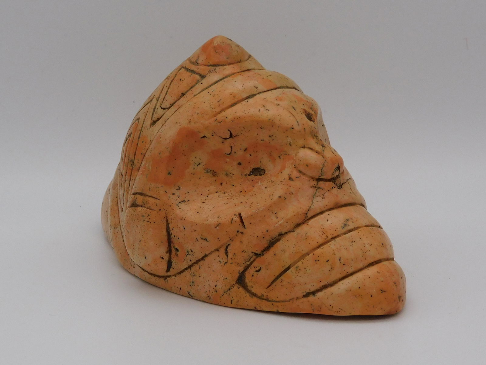 Taino zemi with large eyes and clenched teeth. A: large headband unites the ear spools. Two double beak, bird head symbols are engraved on the back of the cone. Made from a beautiful golden-pink colored jasper. 5 1/2" long. Flat, polished base. Puert