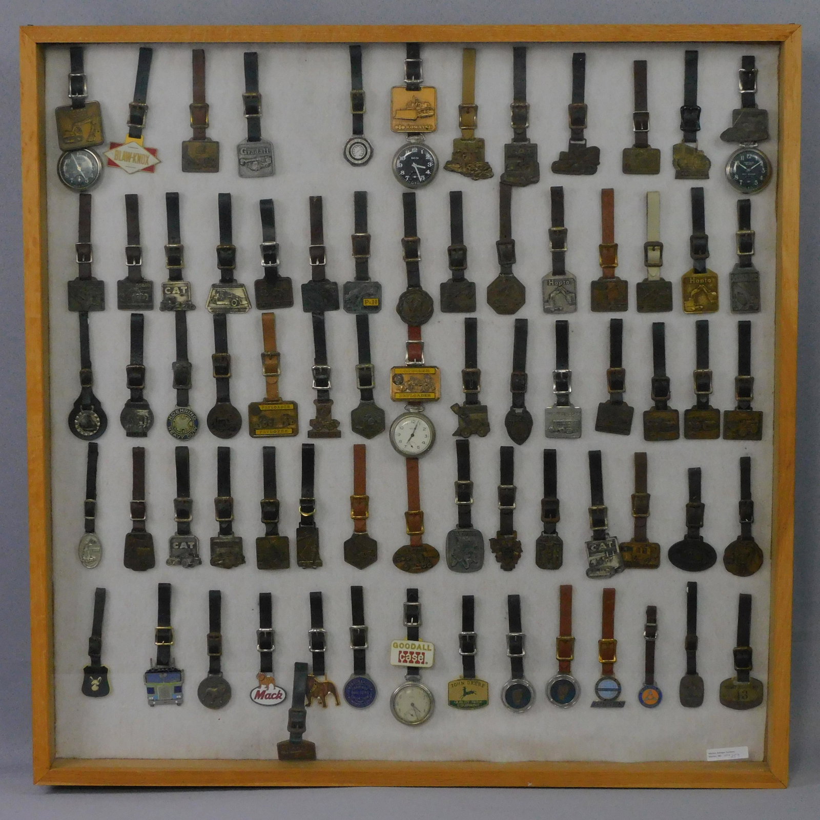 (72) vintage watch fobs with leather straps, in a: hanging glass front case. Representing truck and heavy equipment companies, such as: Case, Gradall, Cat, Mack, Adams, Hopto, P&H, Koehring, Payloader, Sullivan Machinery Co., Lorain, Manitowoc, Caterp