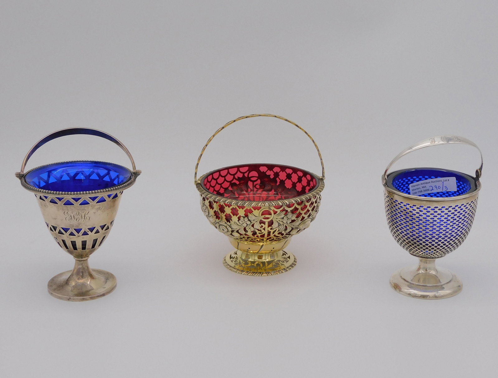 (3) sterling handled baskets with cobalt and: cranberry glass inserts. To include: an English sterling openwork basket with cranberry bowl glass insert with polished bottom, swing handle, grape, floral, and fruit design, gold wash accents, 6" hig
