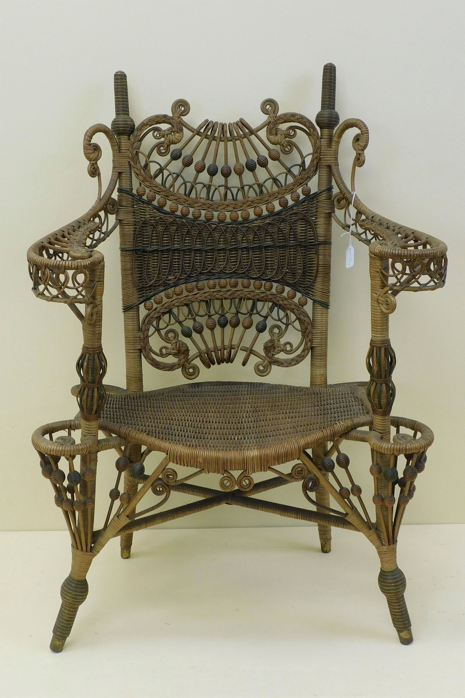Elaborate wicker arm chair by an unknown maker,: 1890. Rattan and wood with bead and curlicued trim. Old natural finish. The armchair has an unusual shaped seat. It features green polychrome paint highlights. 39" high, 27" wide, 17" deep, 16" seat h