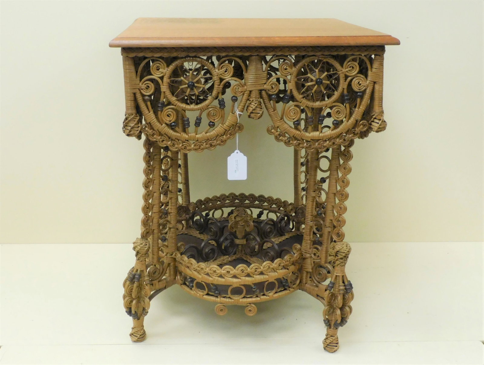 Ornate Victorian wicker parlor table, late 19th: c. Table has a quarter sawn oak top with beveled edge, pinwheel bead and curlicue design. Four section lower shelf. 31" high, 25" wide, 25" deep. Restored natural finish, probably stripped at one poin