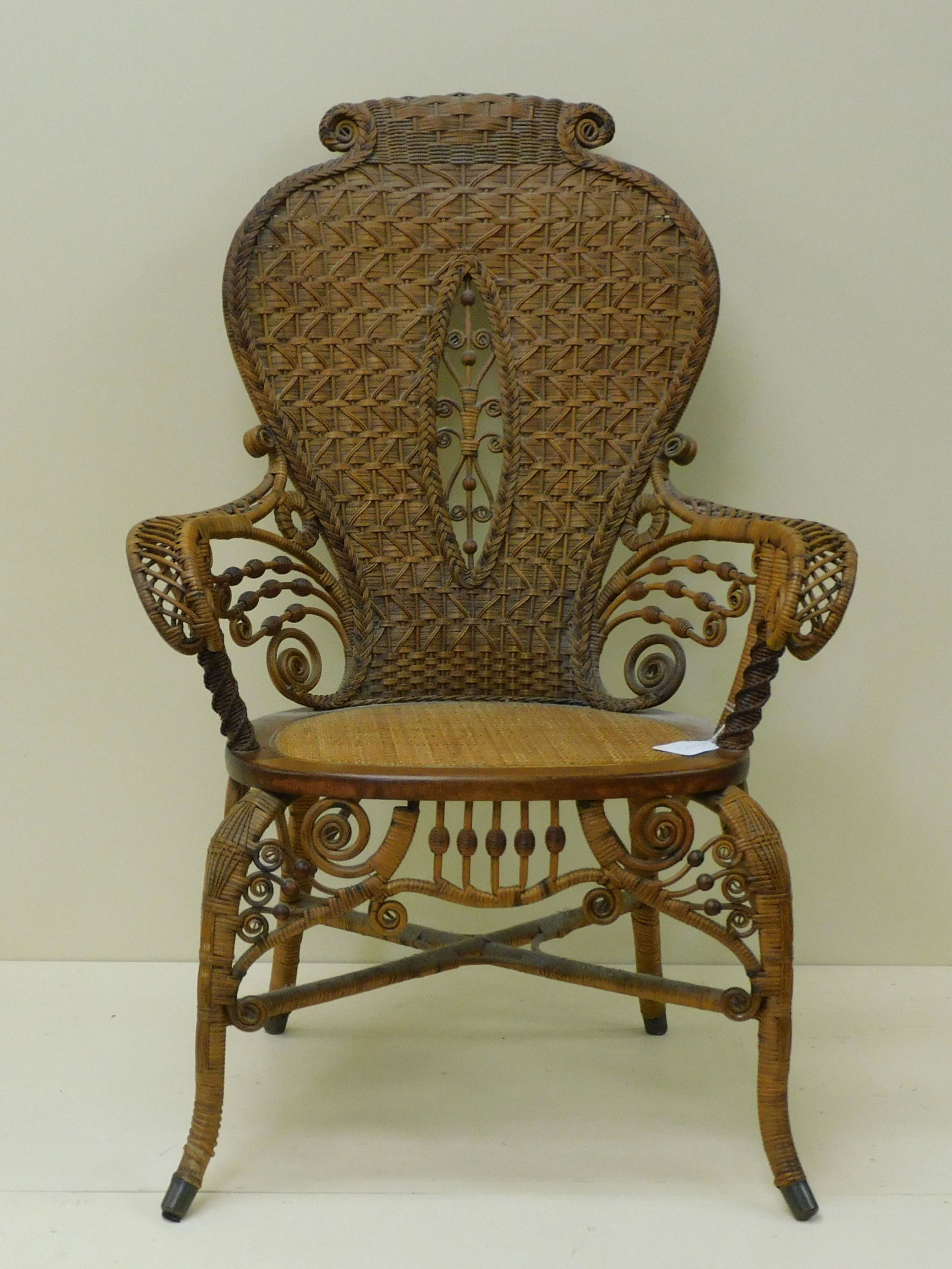 Very scarce ornate Victorian wicker armchair,: late 19th c. Possibly by Heywood Brothers and Wakefield Co. Unusual scroll and shield back design. Chair has an oak frame and cane seat with cabriole legs. 39" high, 27" wide, 17" deep, 16" seat heigh