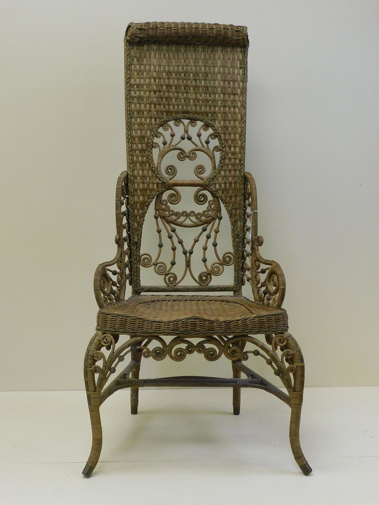 Rare and ornate wicker lady's reception chair,: ca. 1898. Pictured in the Heywood Brothers Wakefield Co. catalog, no. 6516A. Natural finish with polychrome painted highlights, possibly original. Scrolled top crest and ornate central panel with side