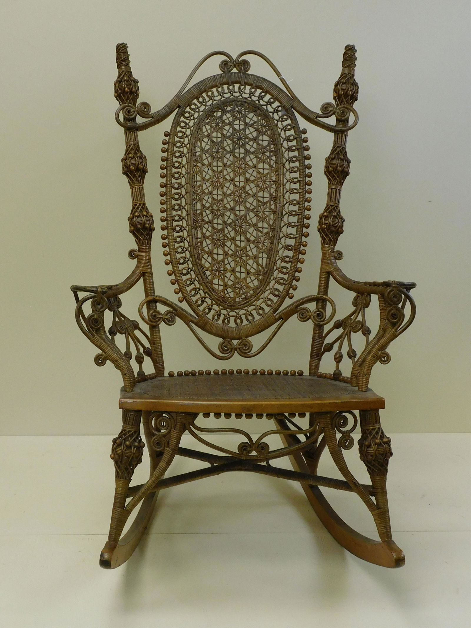 Rare and ornate Victorian wicker gentleman's: rocking chair, late 19th c. Star caned oval panel on the back. Unusual twisted bead designs on post. Maple frame 46" high, 30" wide, 38" deep overall, 20 1/2" seat depth. Original natural finish. Orig
