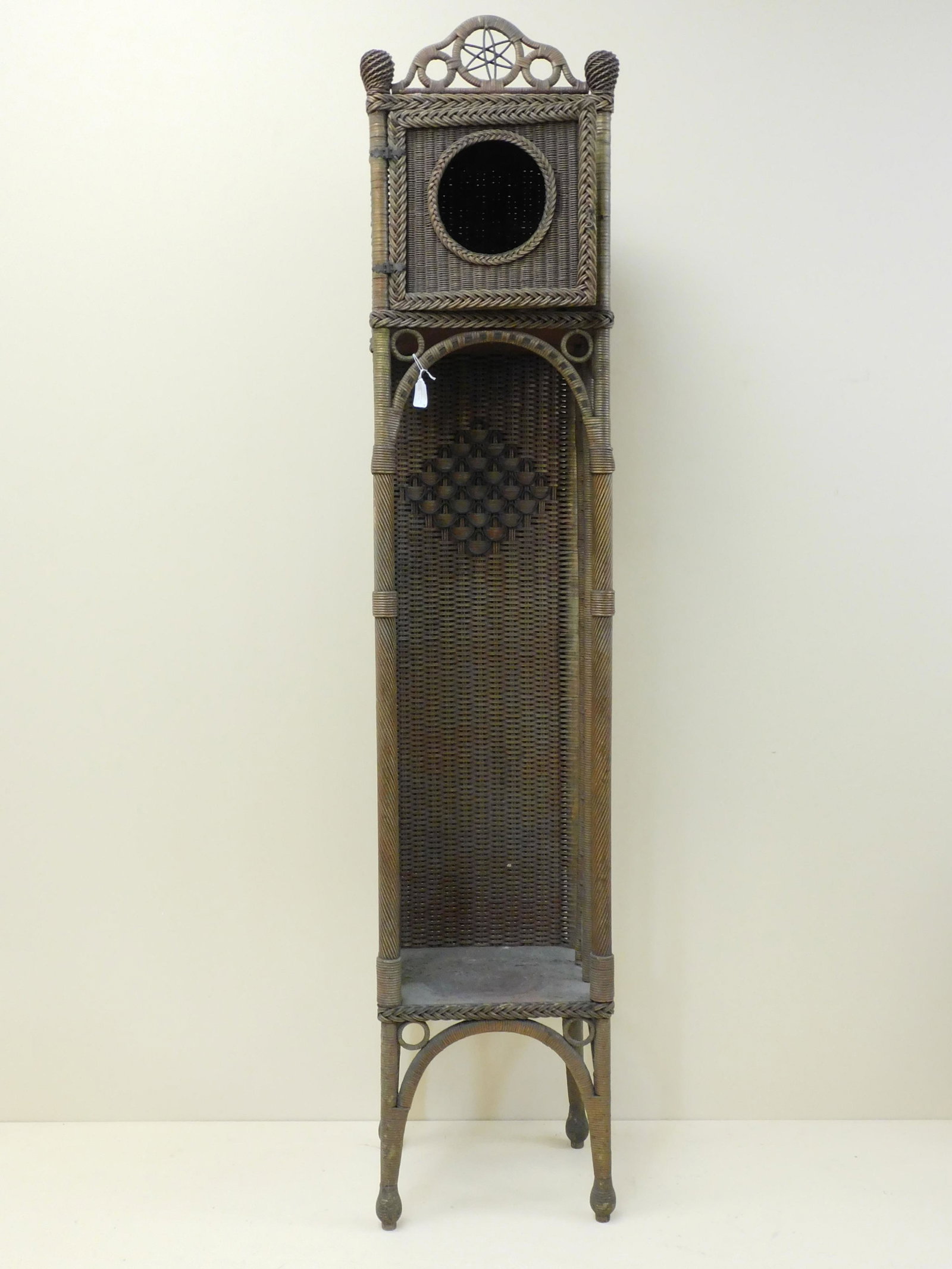 Rare wicker grandfather clock case, ca. 1920.: Original natural finish with polychrome paint highlights. A star crest at top, single door with round window. Deco style scaled design to back panel and upper sides. 77" high, 15" wide, 12" deep. Exce