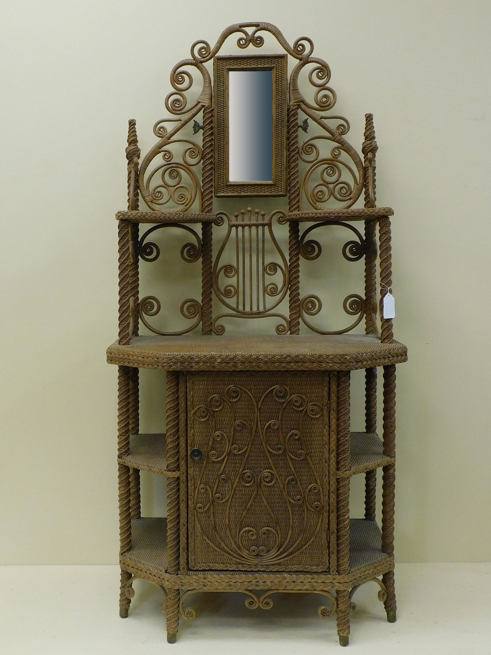 Victorian wicker mirrored etagere / fancy: cabinet, late 19th c. Possibly Heywood Brothers Wakefield Co., MA. Scroll gallery supporting a rectangular beveled mirror, lyre design in back. Single door with applied curlicue design. Six shelves. B