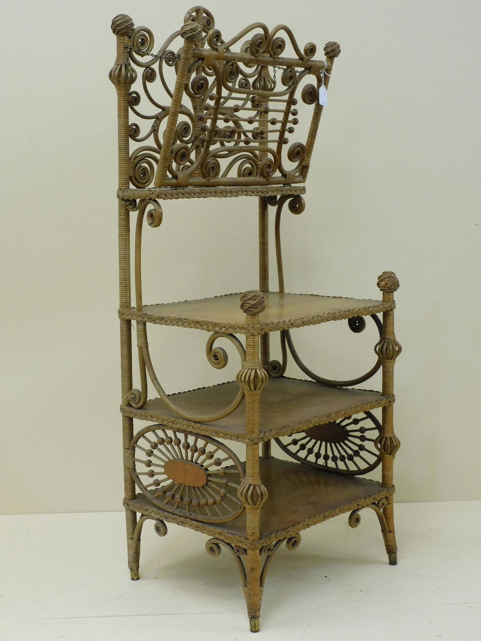 Victorian wicker music stand, Heywood Brothers: Wakefield Co., ca. 1898, no. 6440 in the 1898-99 catalog. Has a fold-out top shelf, with three oak bottom shelves, and fancy twisted rounded finials. Original natural factory finish. 47" high, 18" wid