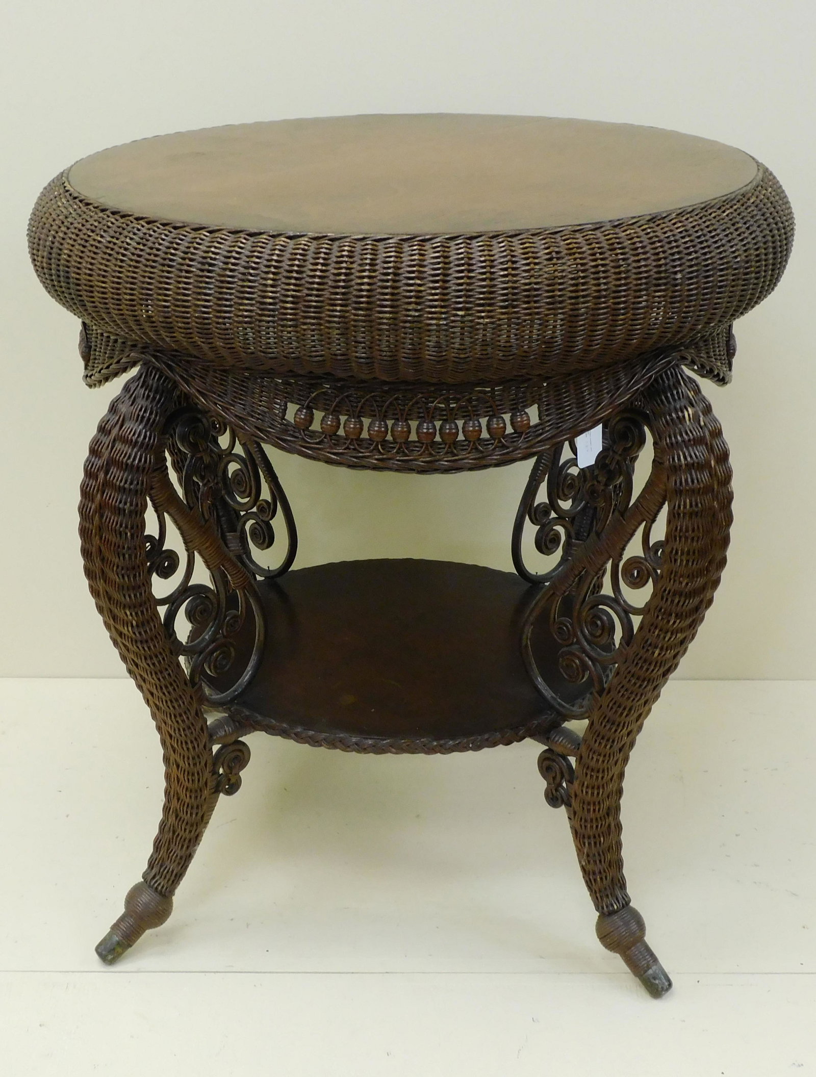 Elaborate Victorian wicker table, Heywood: Wakefield Co., original celluloid label. Ca. 1905. Circular oak top, rolled edge, beaded skirt, cabriole legs with curlicue design, and brass feet. Includes circular oak bottom shelf. 30" high, 29" di