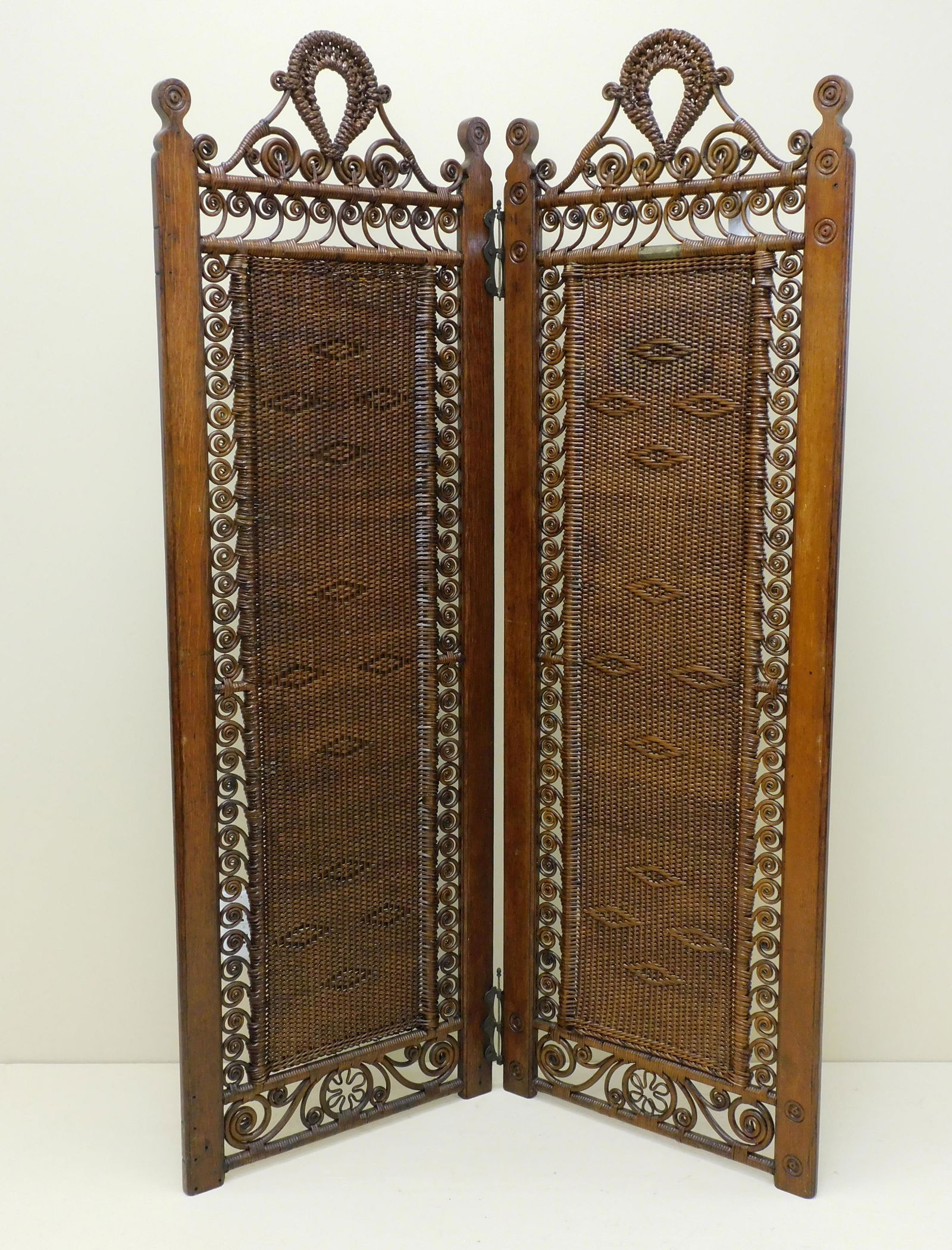 Victorian wicker two-paneled dressing screen,: Wakefield Rattan Co., MA, ca. 1890. Brass labels. Oak and rattan, old natural finish with a light coat of applied polyurethane. Has an elaborate gallery top, closely woven central panels flanked by ro