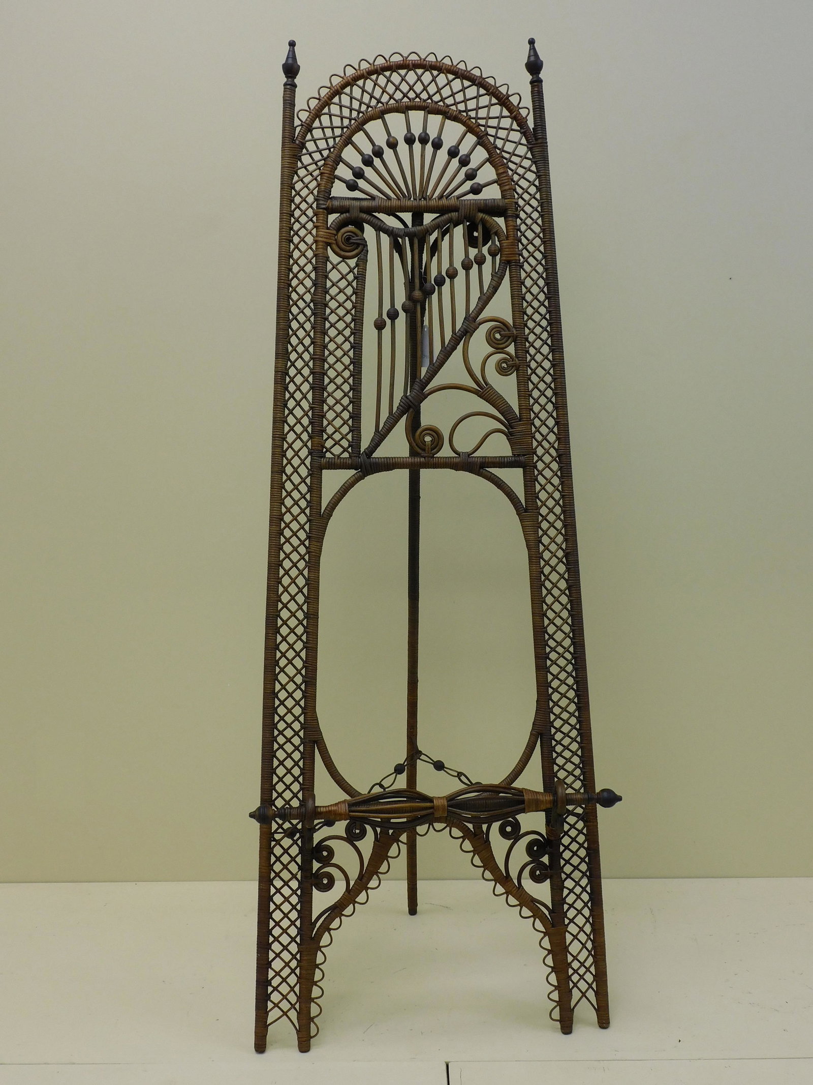 Victorian wicker folding easel, ca. 1890, unknown: maker, probably Massachusetts. Original natural finish. Harp design in upper center, elaborate bird cage supporting stand at bottom. 61" high, 23" wide, 16 1/2" deep when open. Shows some areas of old