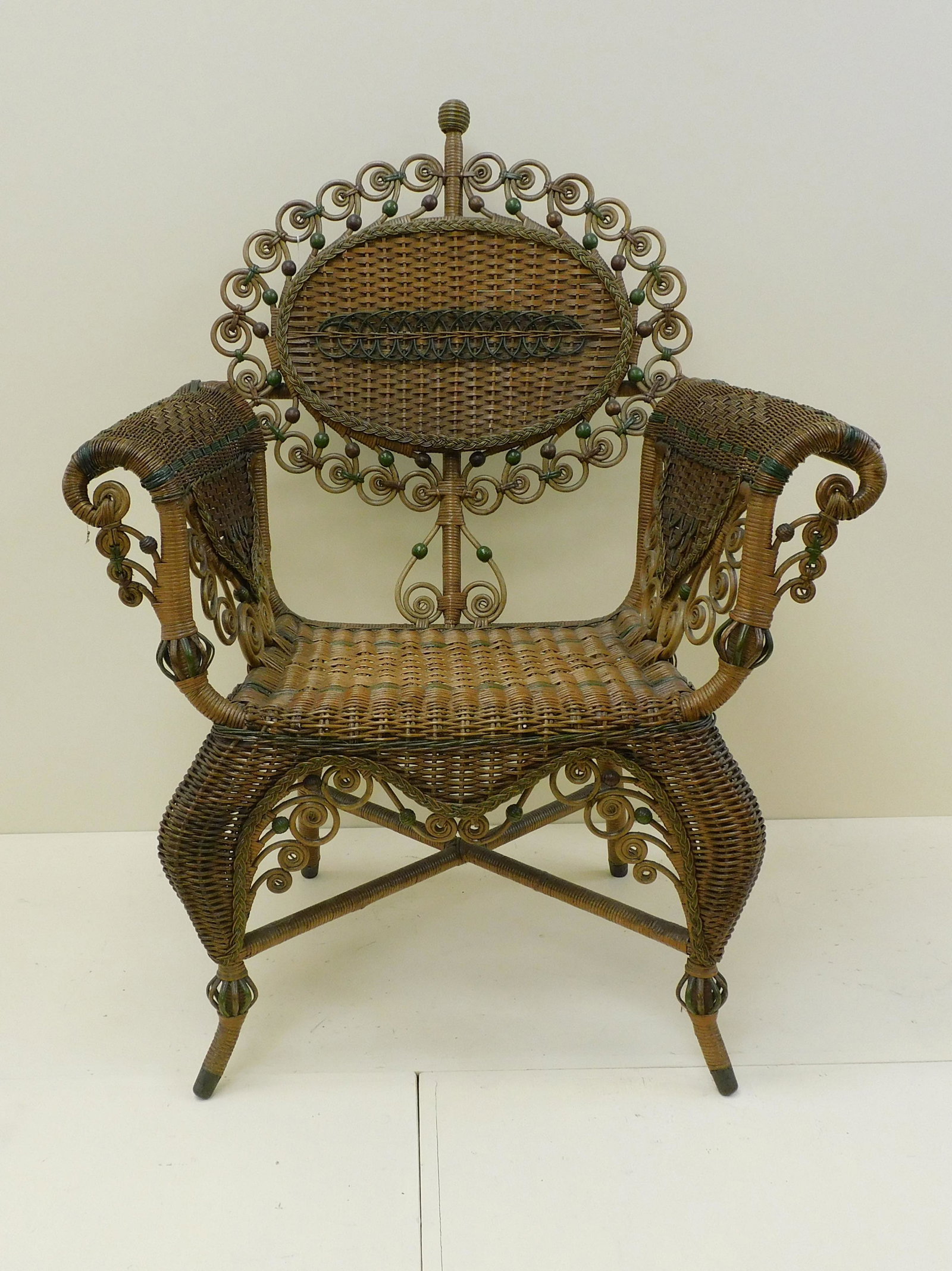 Victorian wicker arm chair, ca. 1890. Rattan with: hardwood frame, unknown maker, probably MA. Original natural finish with green polychrome paint highlights. Oval back surrounded by a curlicue gallery. Rolled arms, cabriole legs. 40 1/2" high, 30 1/2