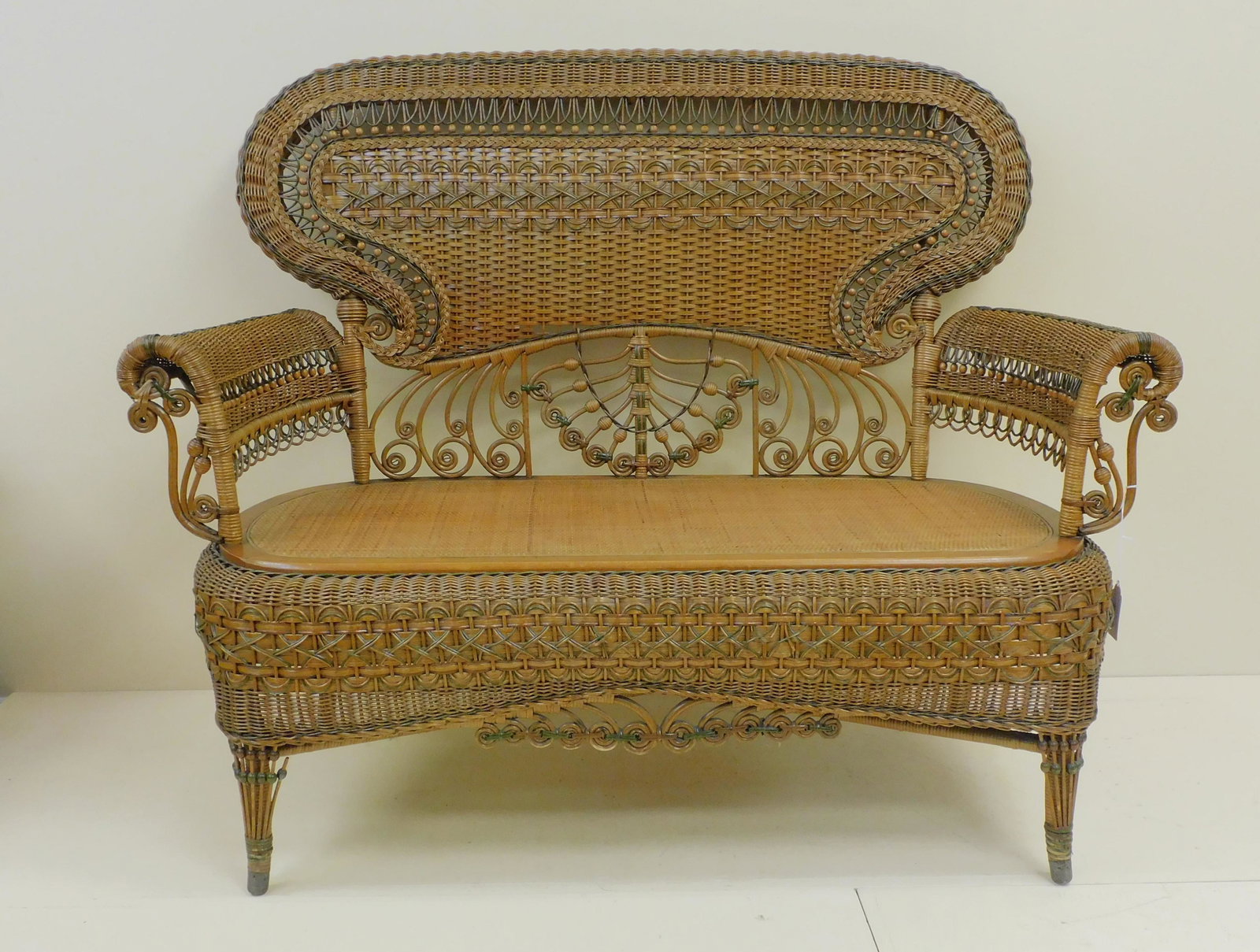 Victorian wicker settee or tete-a-tete, Heywood: Brothers Wakefield Co., ca. 1898, no. 6078F on p. 67 of the Company Catalog. Rolled back and arms, pressed cane seat, maple frame. Original natural finish with green painted highlights. Original facto