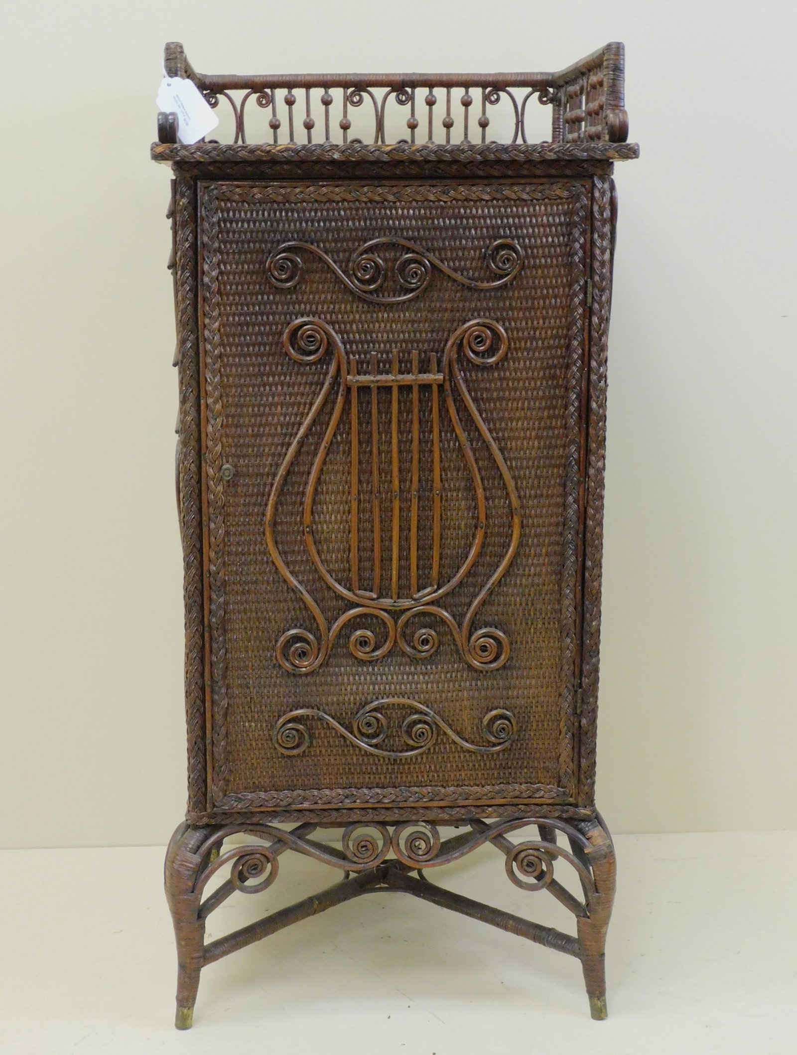 Extremely rare music cabinet, Heywood Brothers: Wakefield Company, ca. 1898. Original label on bottom. Oak and rattan. Beaded and curlicue gallery, rectangular door with applied curls and lyre motifs. Also applied musical scale and notes on sides. 