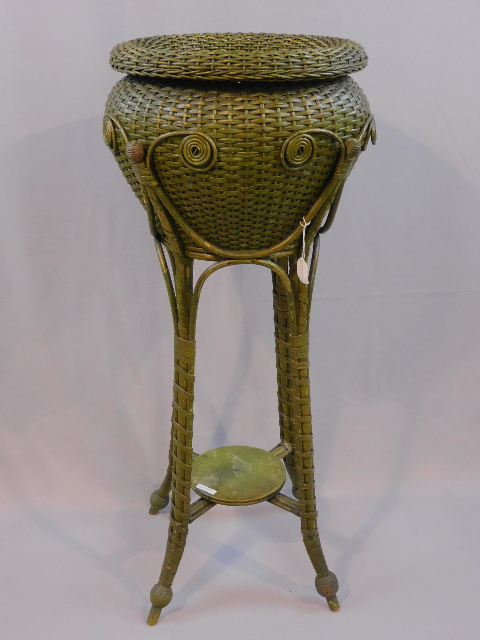 Victorian wicker plant stand, ca. 1890. Original: green paint. Curlicue design. Good condition, with minor paint loss. 42" high, 19" diameter. Provenance: Mary Jean McLaughlin Collection.