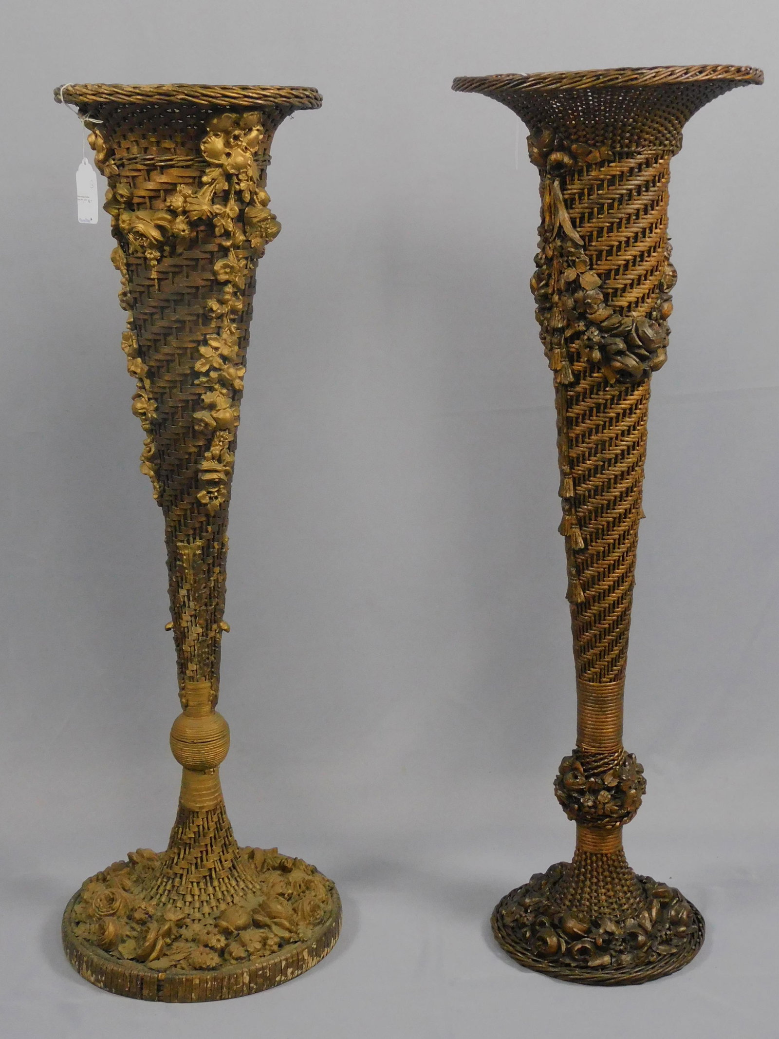 (2) similar wicker floor vases, ca. 1920. Trumpet: form with applied floral design. Metal liners. Original finish. Minor loss to floral gesso on one. Both are 42" high, one is 12" diameter, the other is 13 1/2" diameter. Provenance: Mary Jean McLaughl