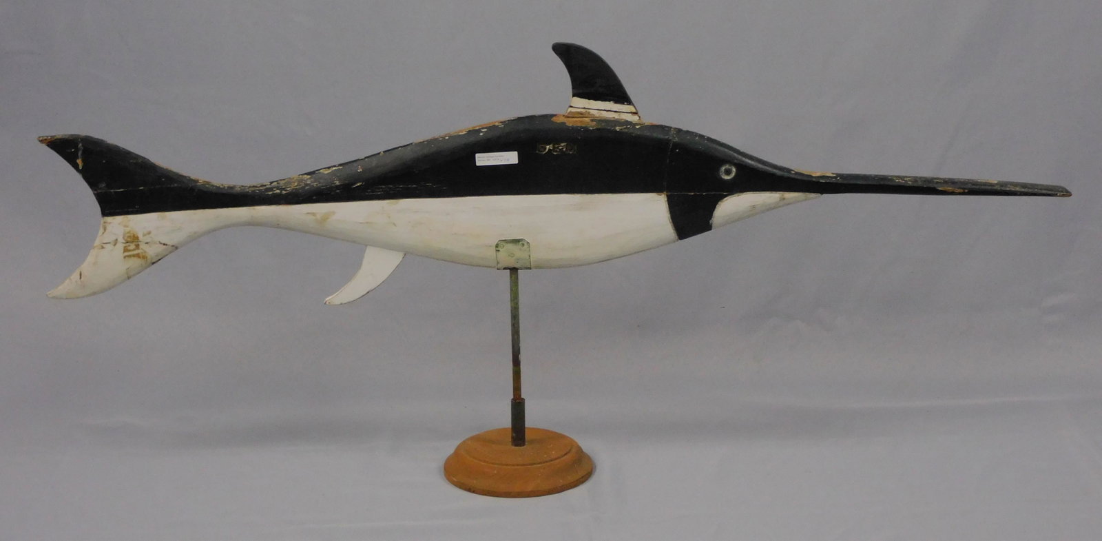 Swordfish weathervane, 20th c. Carved wood, old: painted finish. Signed DEM. Mounted with an iron rod on a modern wooden base. Shows several areas of paint loss. 19" high with its stand, 44" long. 6 1/2" base diameter.
