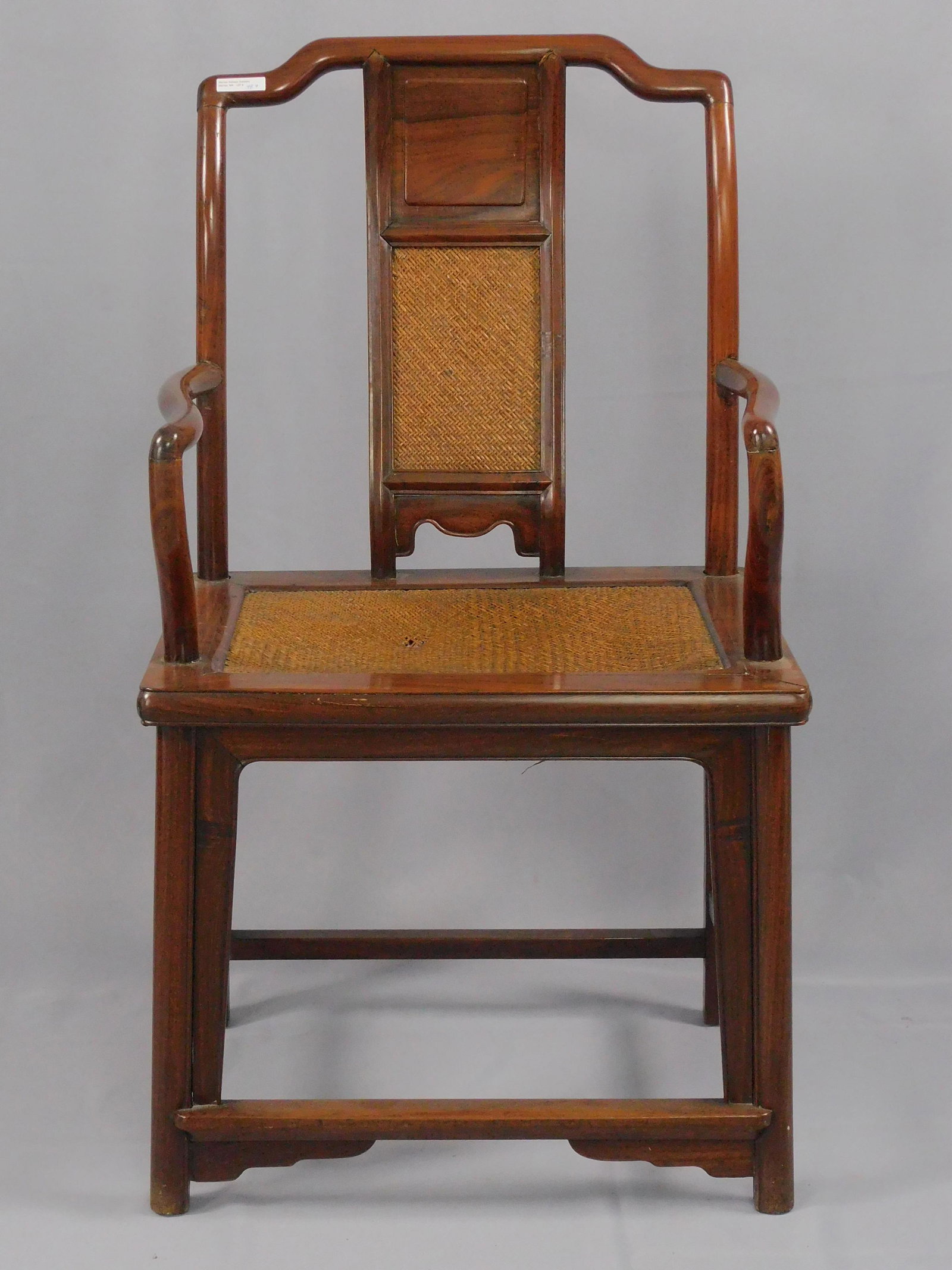 Chinese huanghuali armchair, early 20th c. Woven: back and seat panels. 39" high, 21" wide, 16 1/2" deep, 18 1/2" seat height. Seat panel shows damage. Shows several well done old repairs. A replaced corbel on the rear skirt. Provenance: featured in 