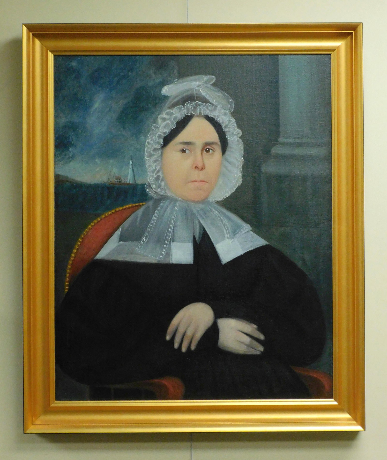 Portrait of a ship captain's wife, ca. 1835. Oil: painting on canvas of Mrs. Francis Moore of Bristol, RI. The painting is set in a modern gilded frame. Mrs. Moore is dressed in black, wearing a lace cap, seated in a red upholstered chair. Behind her