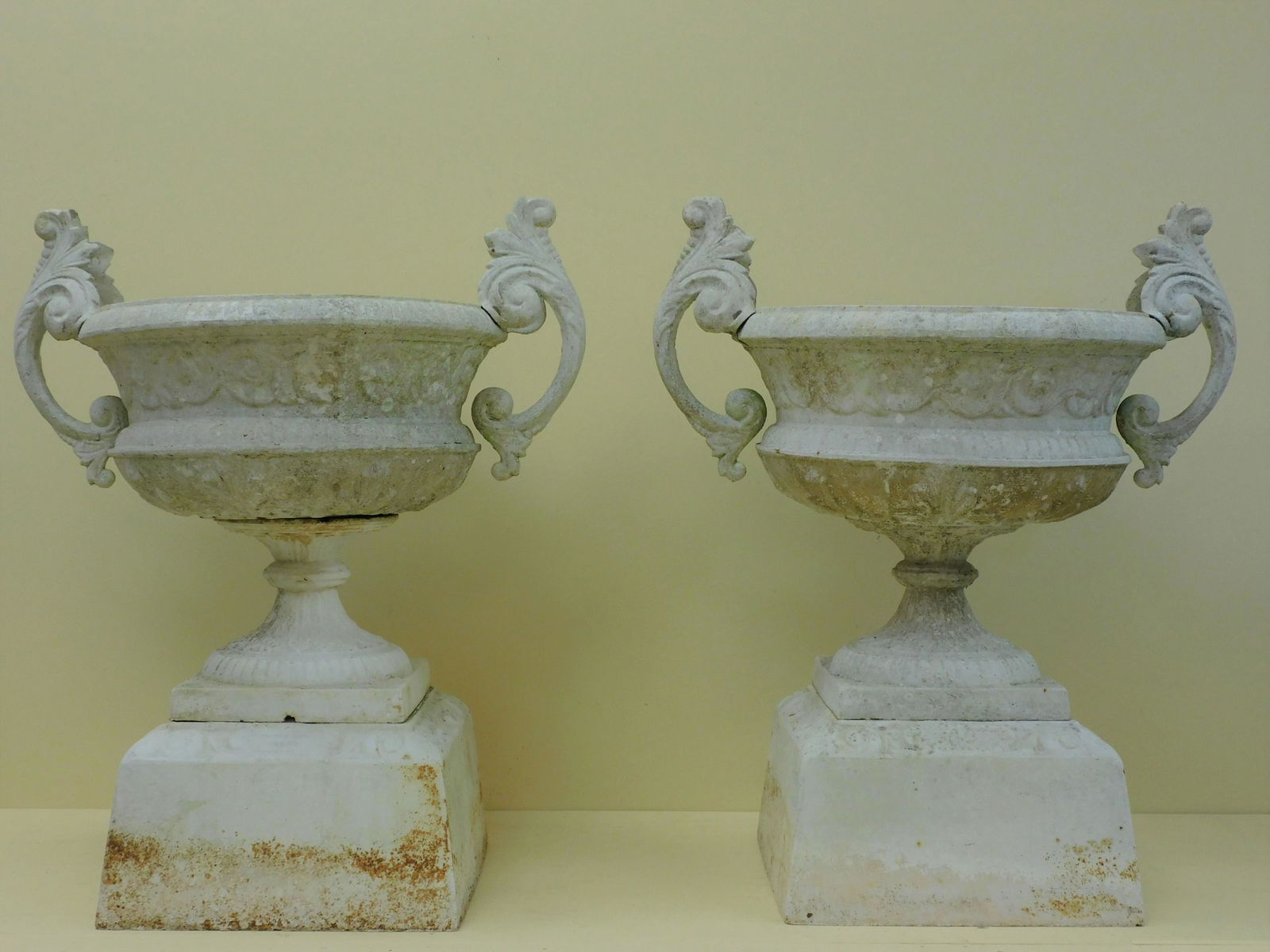 Pair of Kramer Bros. Foundry cast iron three-part: urns. Late 19th century. Zinc handles. White painted finish. Shows traces of multiple coats of paint, some rust. As-found garden condition. 34" high, 28" wide, 20 1/2" diameter.