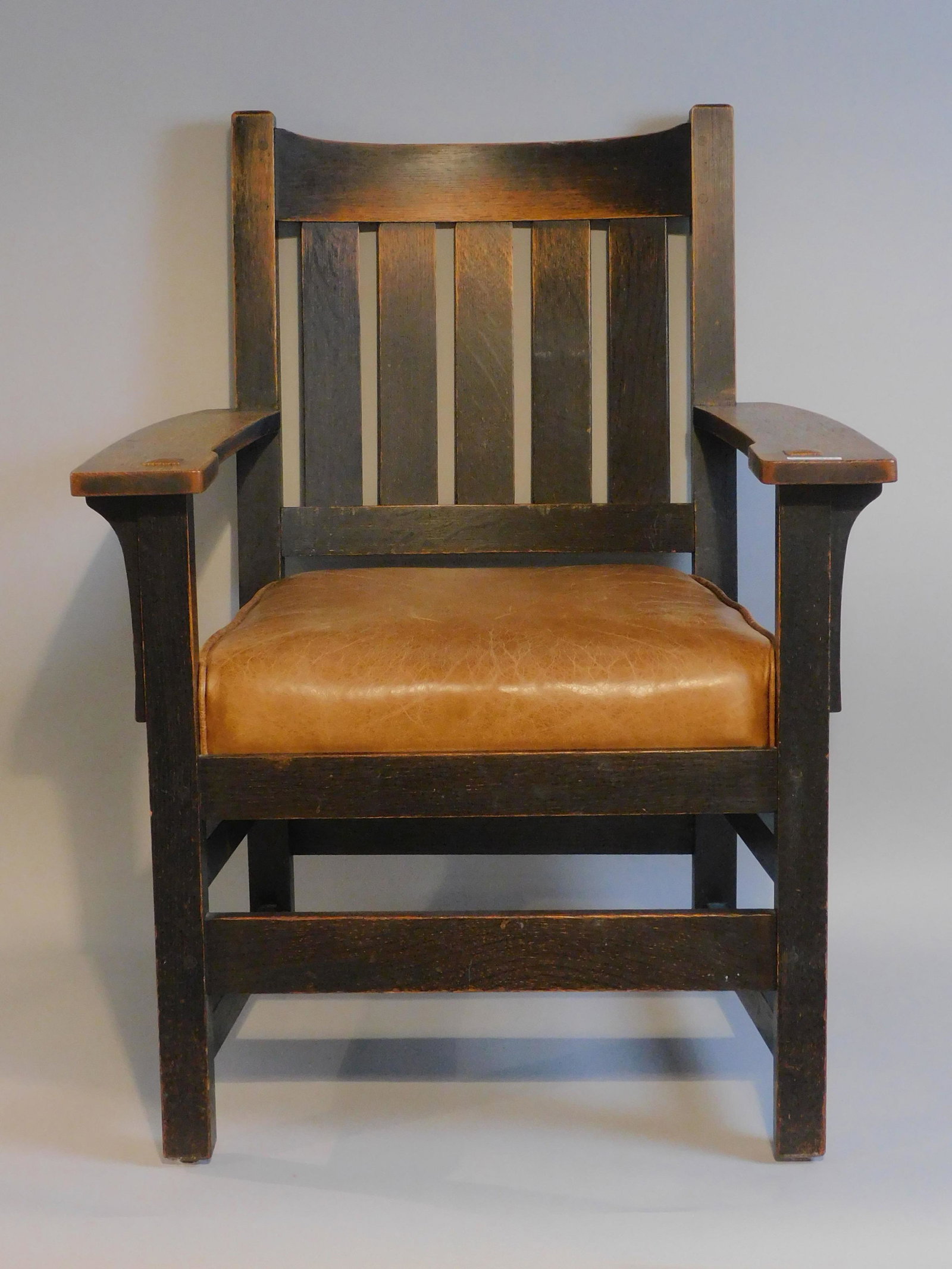 L & J G Stickley armchair, ca. 1910. Slat back,: old dark finish. Leather seat, original label. 35 1/2" high, 27" wide, 20" deep. Good overall condition. Peg construction.