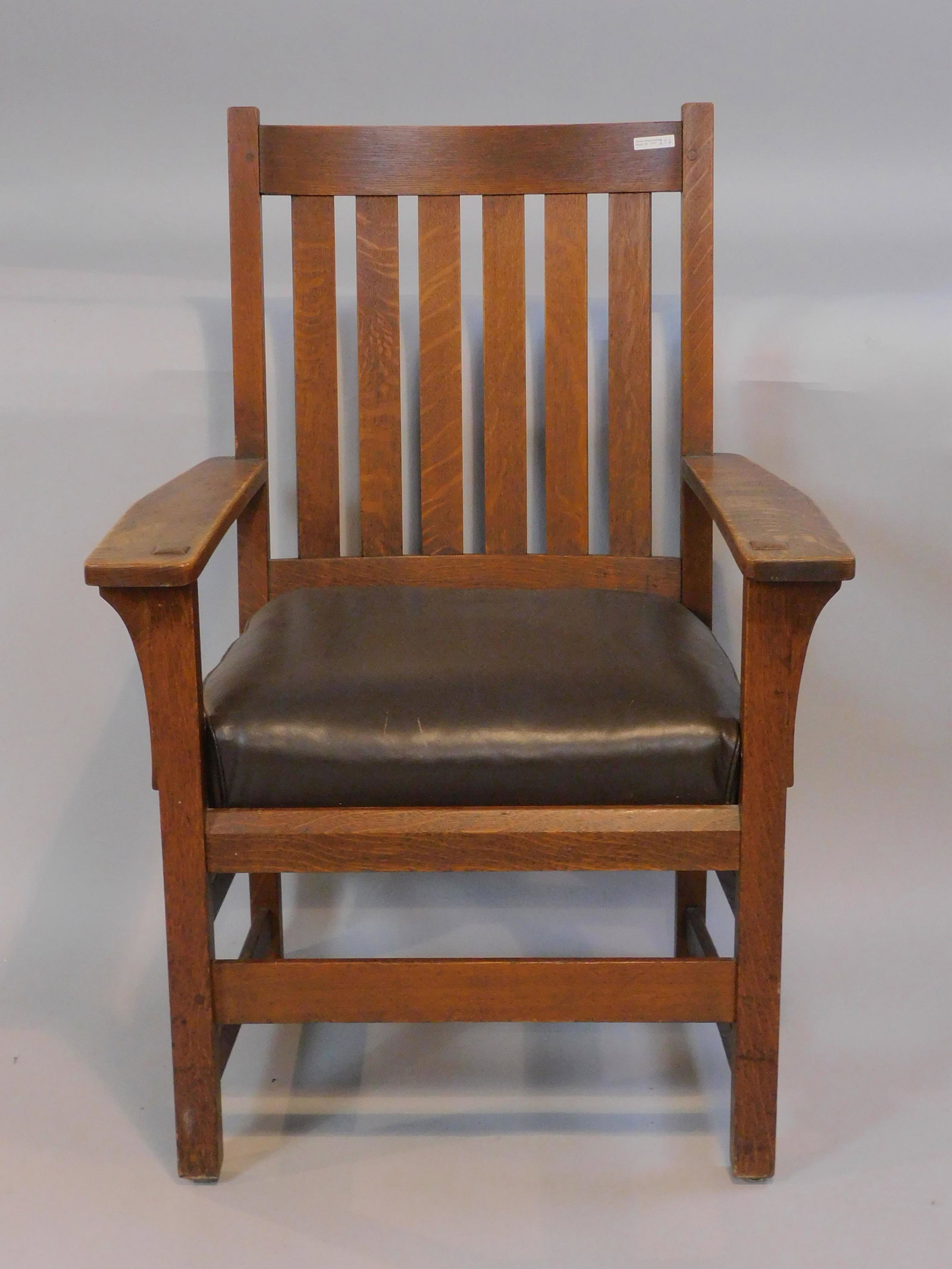 Stickley armchair, ca. 1910, slat back, peg: construction. Original label with clamp. Old finish, leather cushion. 39" high, 27" wide, 21" deep.