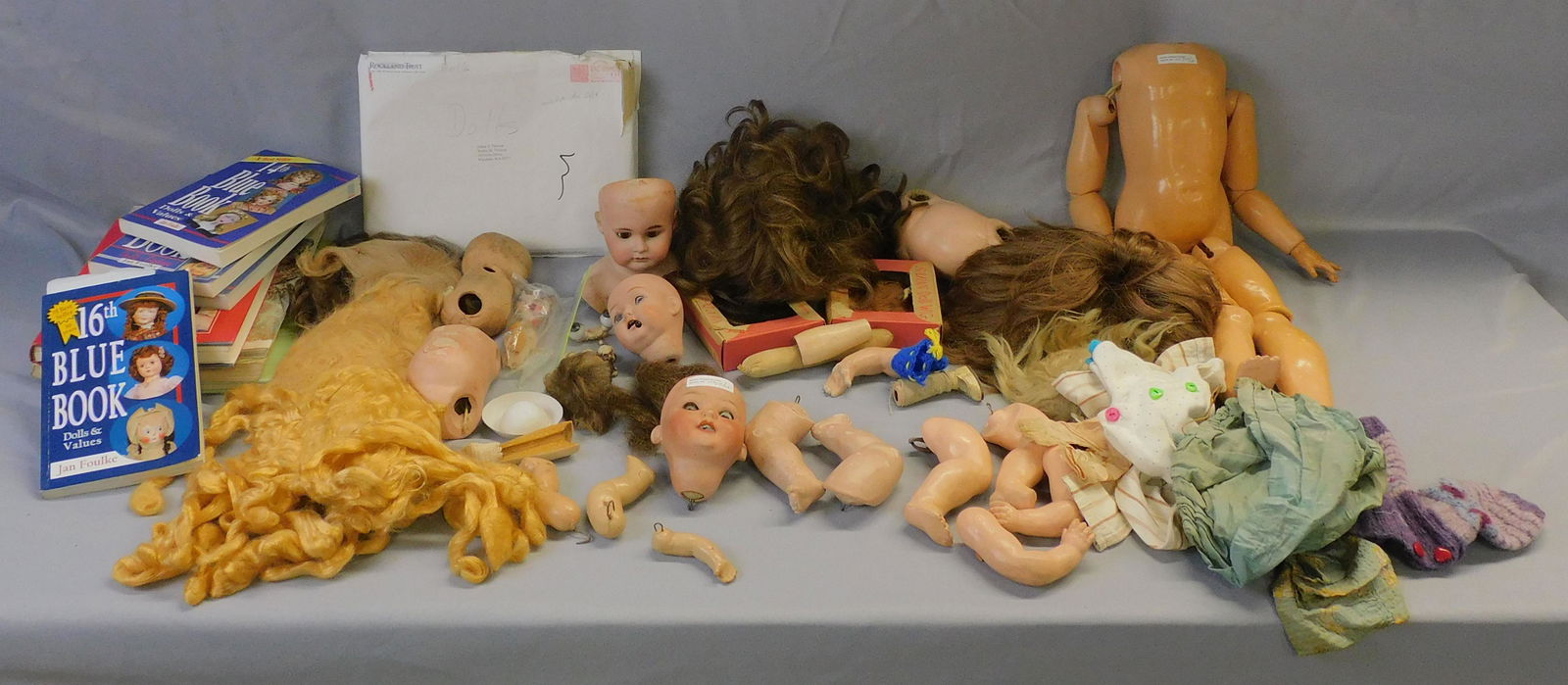 Collection of doll parts, wigs, books, and a few: pieces of miscellaneous clothing. Bisque heads, some as-is. Composition bodies, limbs.
