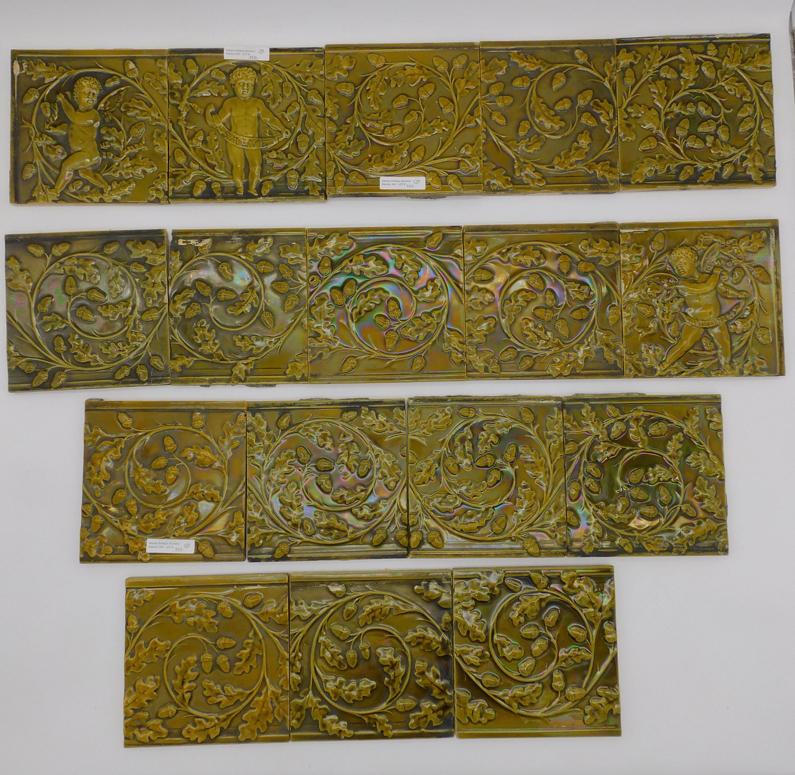 (17) Minton Hollins & Co tiles, Stoke-on-Trent.: Three cherub tiles, one holding a banner which reads "salve". 14 other tiles with embossed oak leaves, vine and acorn design. 6" x 6". Dark green tin glaze.