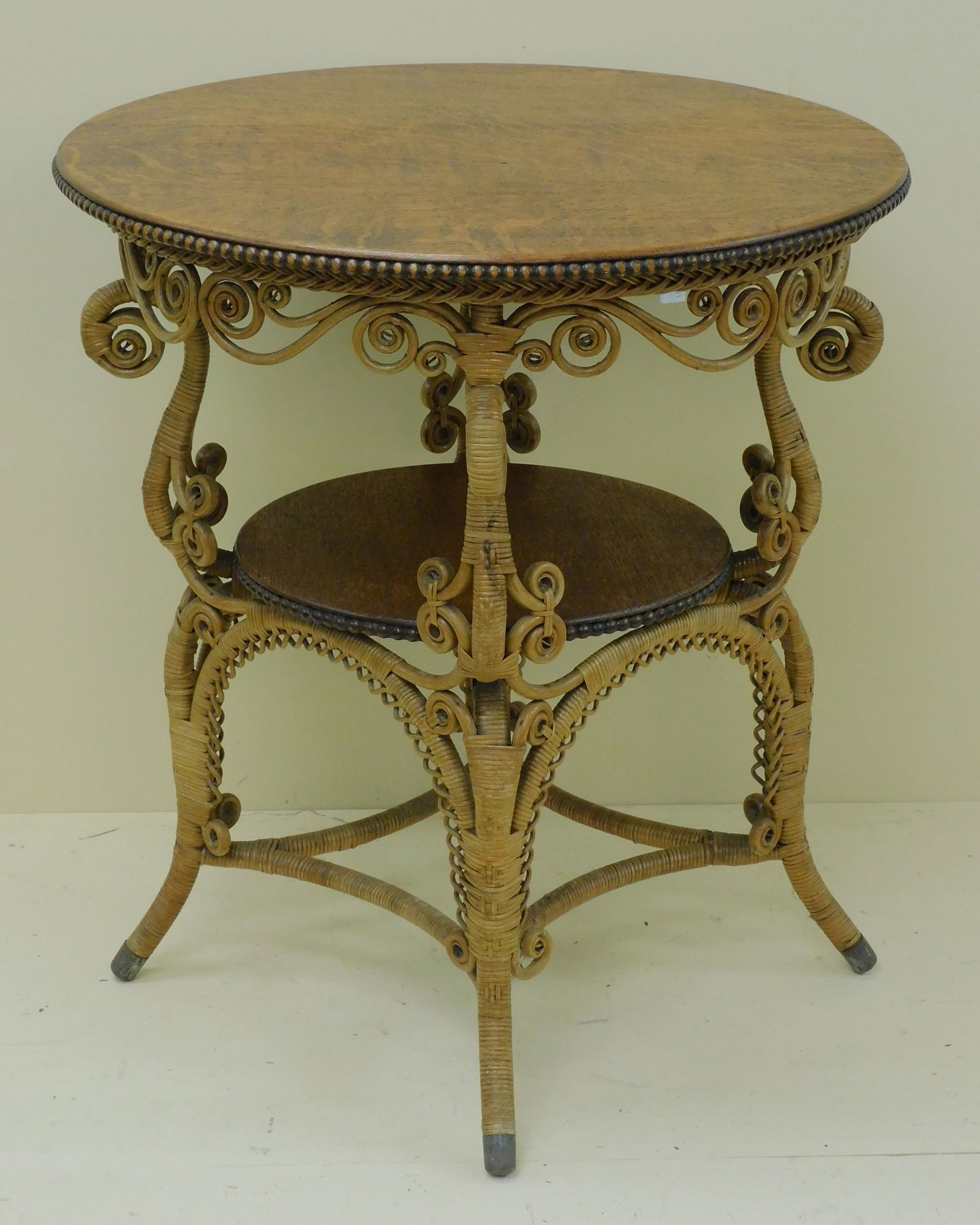 Victorian wicker two-tiered lamp table, ca. 1890.: Quartersawn oak top with beaded trim. Curlicue design. Original natural finish. Excellent original condition. 30" high, 26 1/2" diameter. Provenance: Mary Jean McLaughlin Collection.