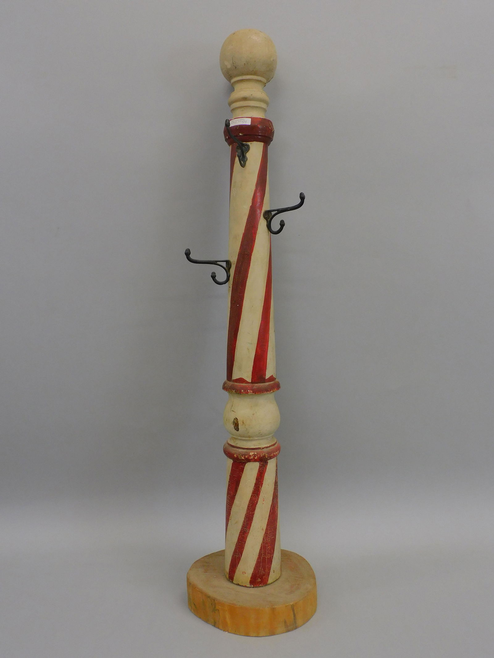 Folk art barber pole. Late 19th century. Turned: wood and painted barber pole mounted on a round wood slab. Currently used as a child's coat rack. 45 1/2" x 4 3/4" dia. The base shows a split in the wood. The pole shows minor paint loss