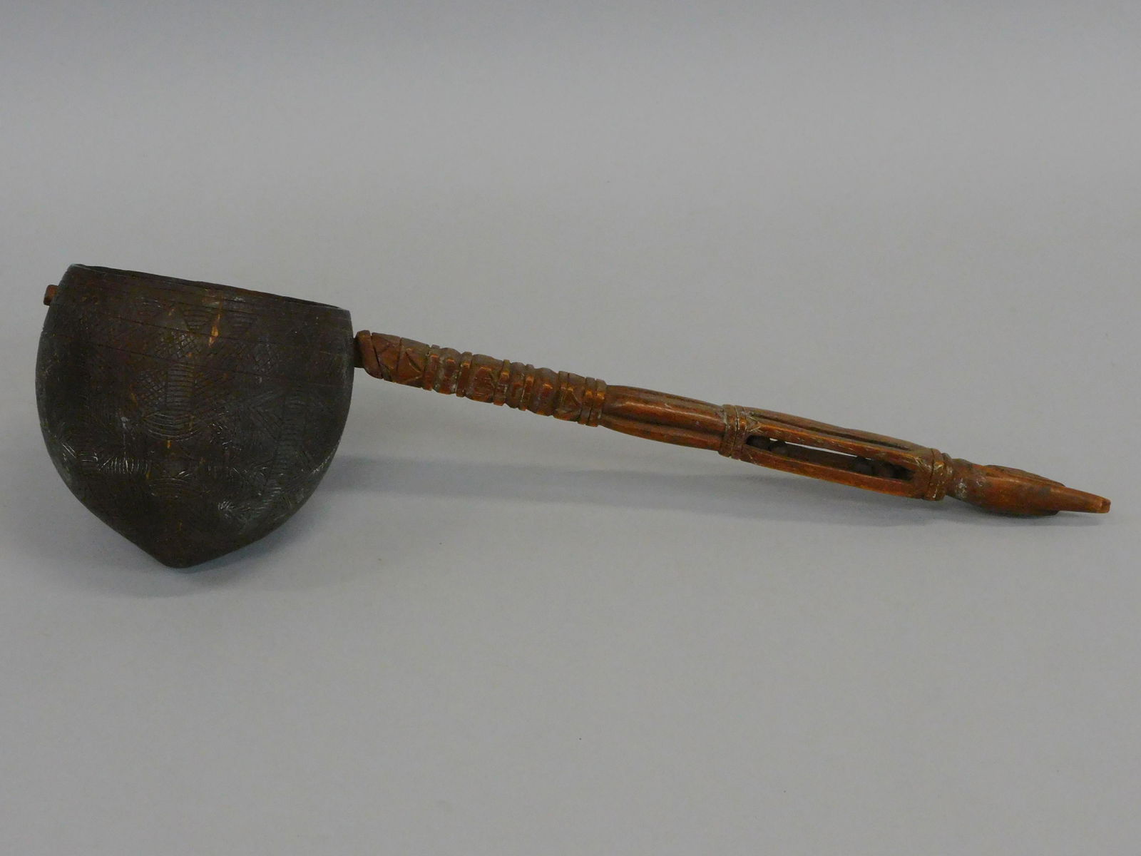A folk art coconut dipper. Mid 19th century.: Sailor made. A thumbs up finial with puzzle ball and geometric carved shaft. Coconut shows extensive incised, geometric carvings with original natural finish. 15 1/2" x 4 1/4" x 4". Excellent overall