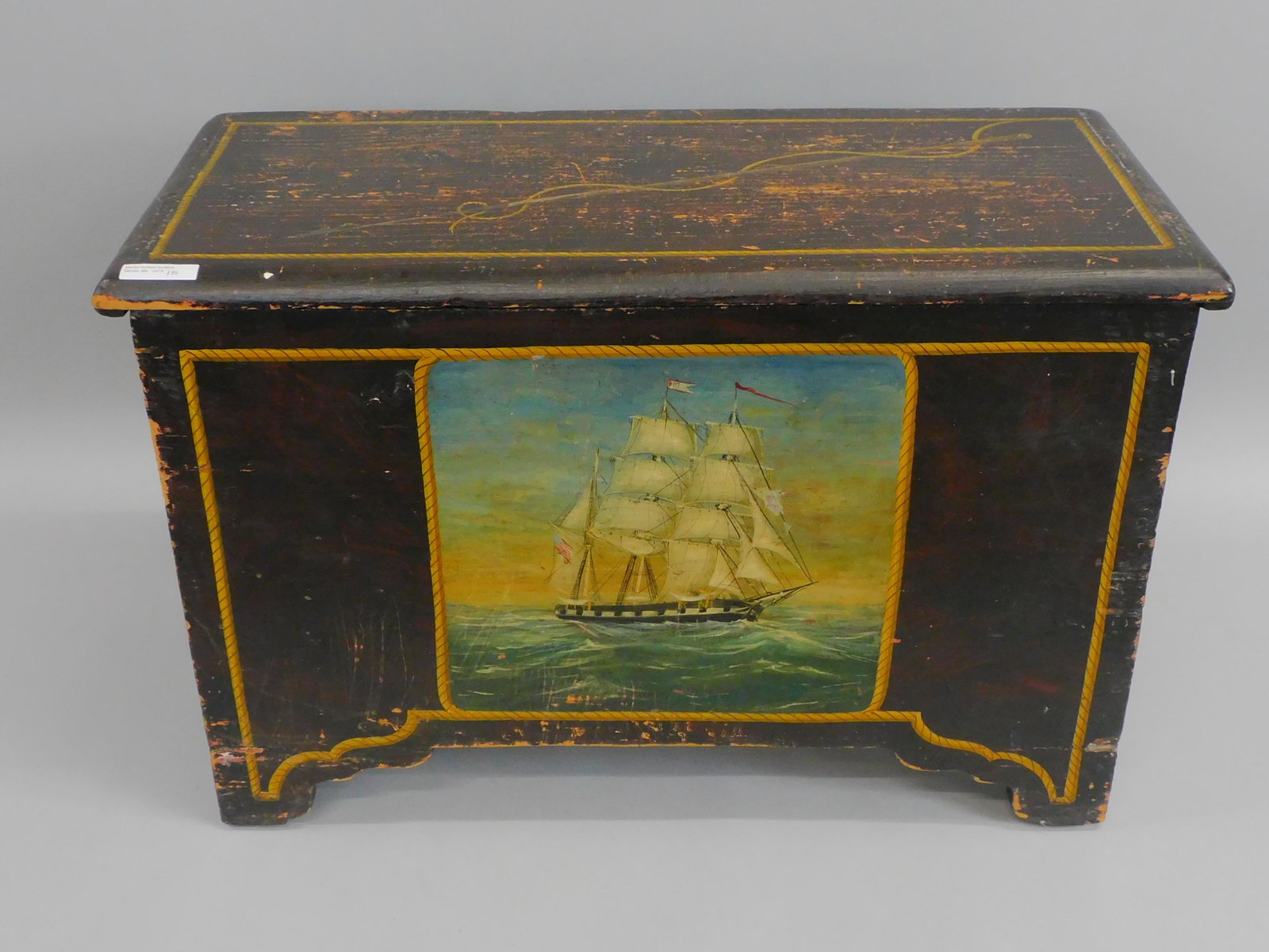 Miniature (6) board blanket chest. Early 19th: century. Made of pine with a grain painted surface. The lid shows a later painting of a harpoon with a rope and rope border. The front shows a later painted American 3 masted ship under full sail with