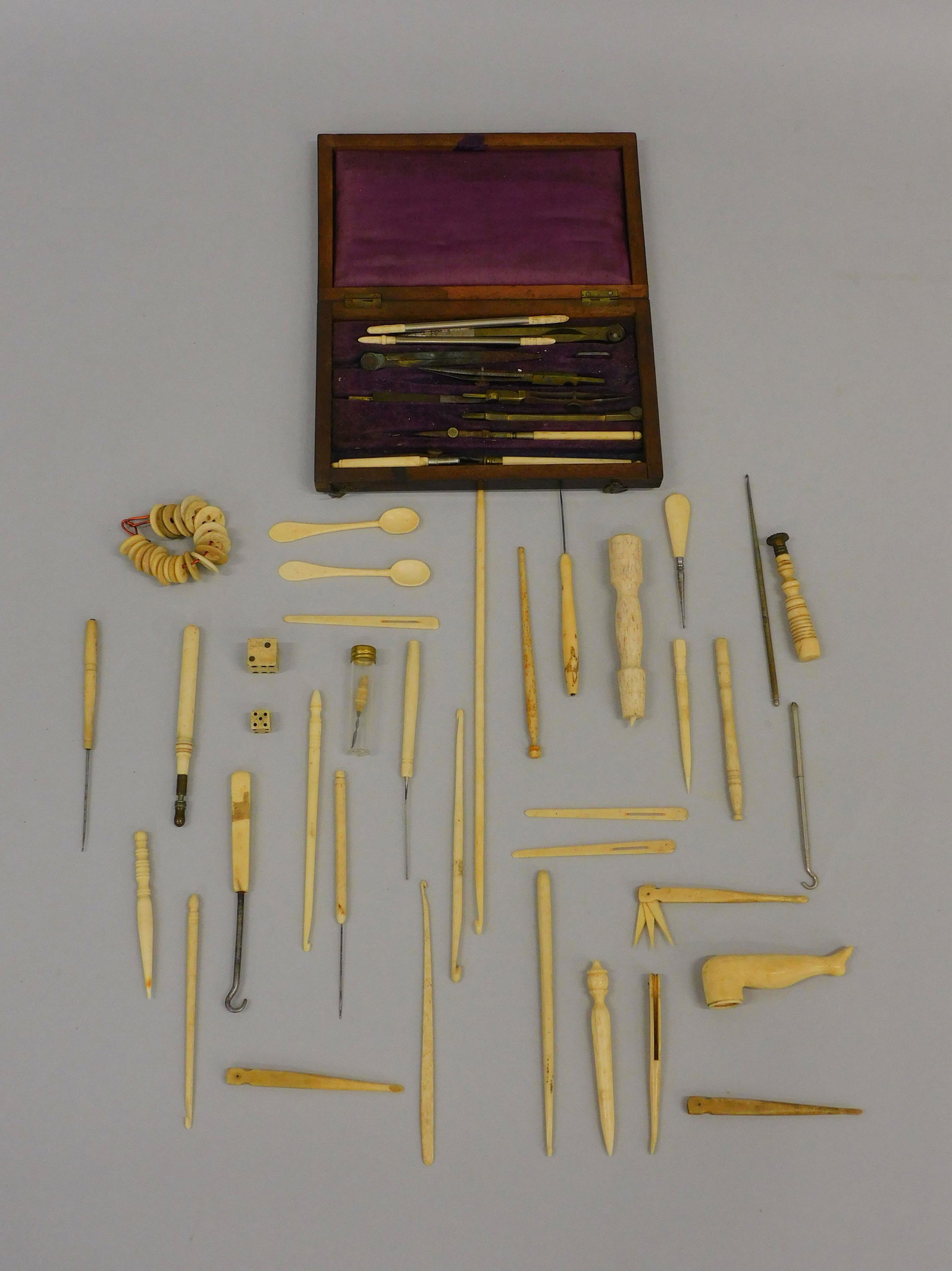 (65) scrimshaw implements. 19th c. To include: carved knitting needle with foot, bone dice, drafting set in a fitted wood mahogany case, bone buttons, seal, spoons marked France. Various sizes ranging from 1 1/2" to 9". Good condition.