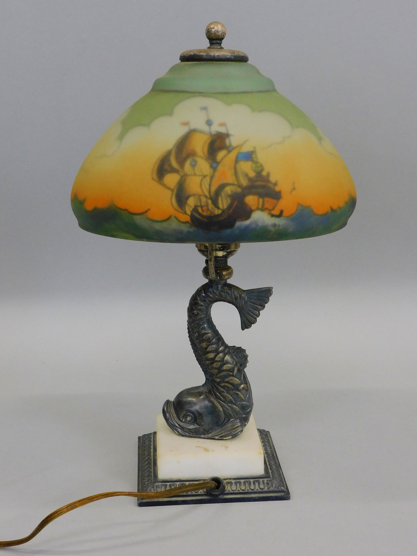 Pairpoint boudoir lamp, circa 1915. Reverse: painted shade. Nautical scene with ship under sail. Exceptional dolphin form silver plated base, marble plinth. Excellent original condition. Lamp is signed on base. 14 1/2" high, approx 8" diameter.