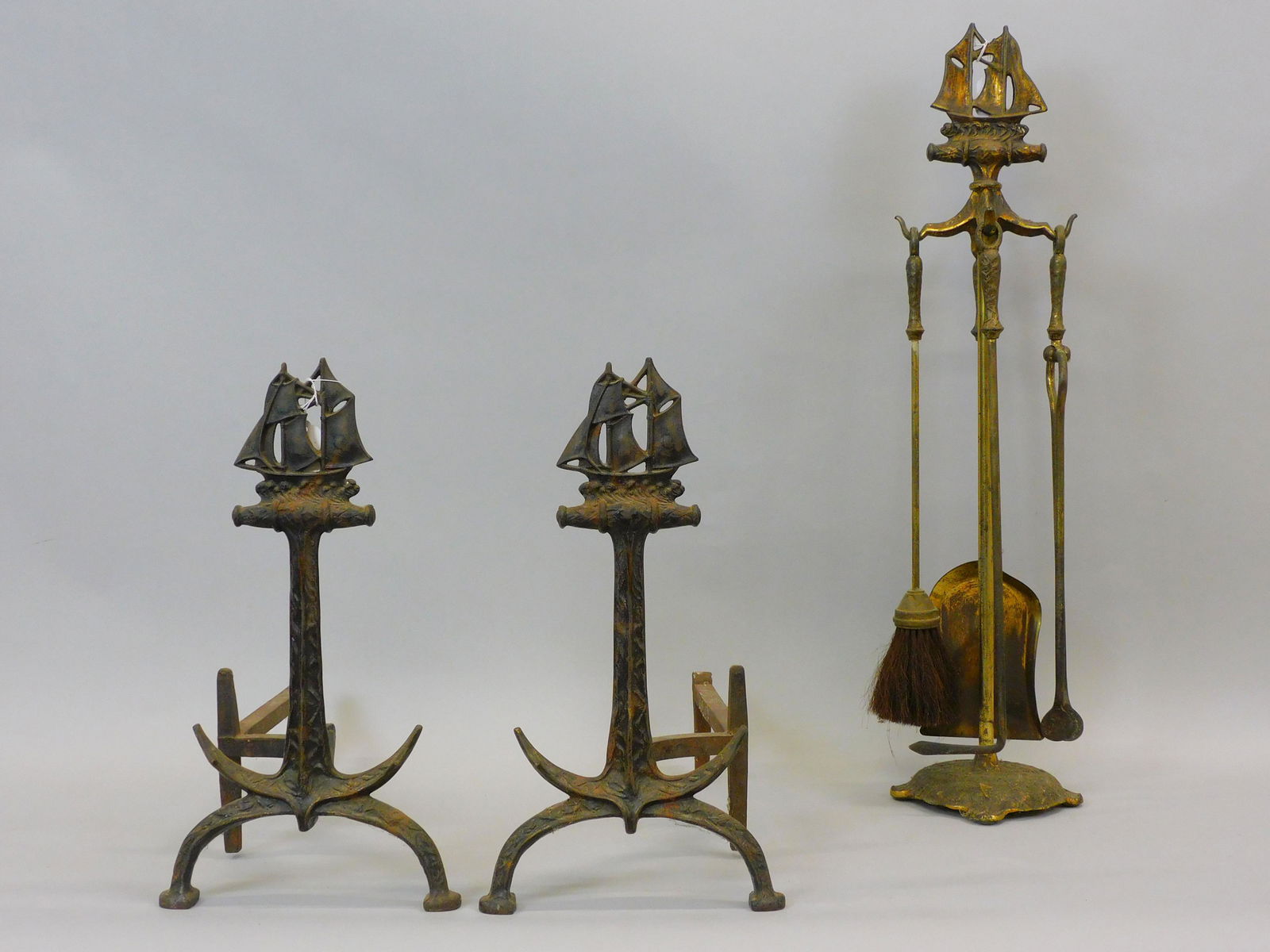 Nautical cast iron fireplace set. Early 20th: century. A pair of andirons featuring a schooner atop of an anchor. Slot in dog design. 18 3/4" x 10 1/2" x 19" Set of (4) cast iron and brass finish fire tools and holder with shovel, tongs, brush, a