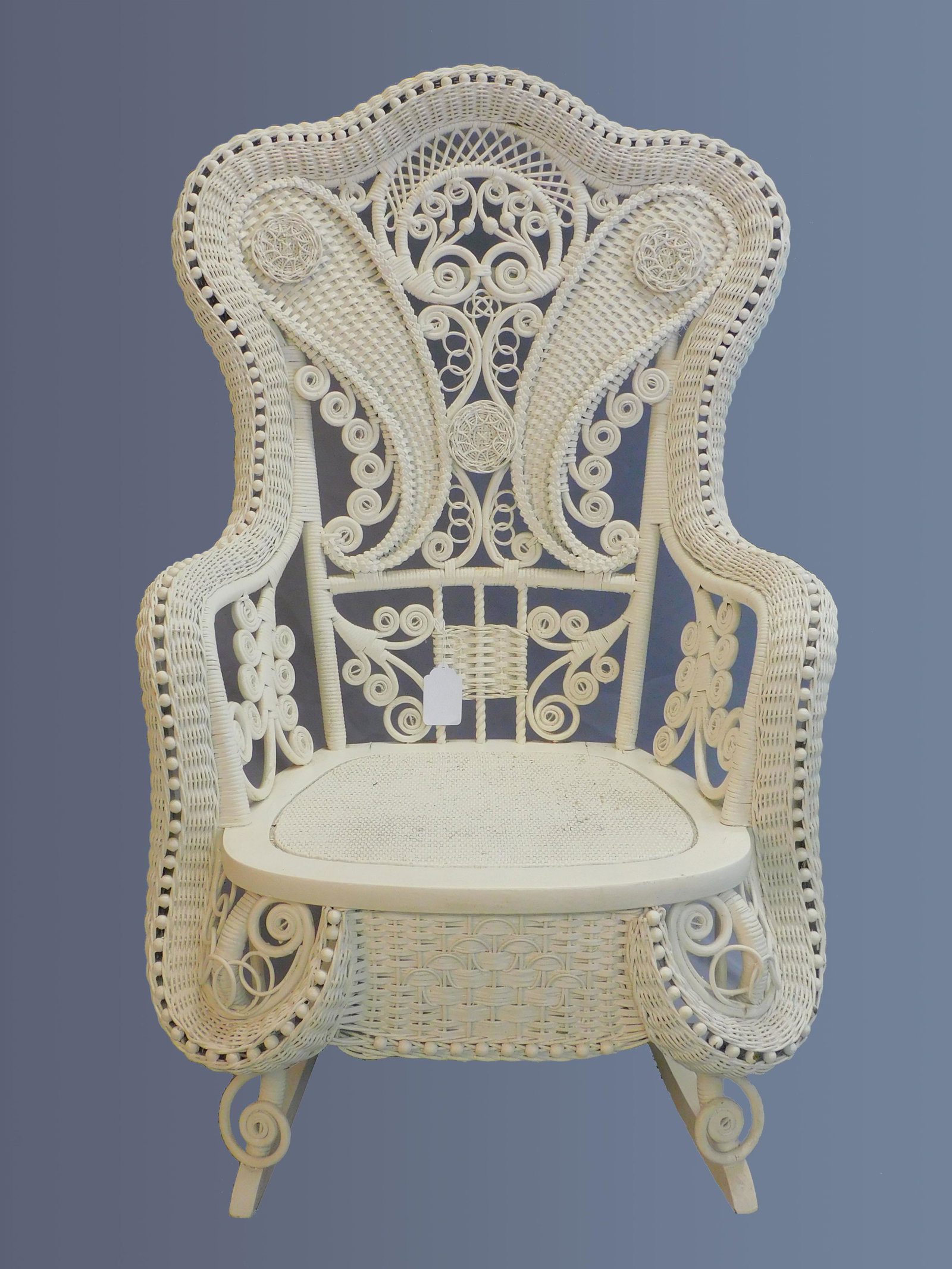 Victorian wicker rocker. Circa 1890. Elaborate: rolled and beaded design. Old white painted finish. Very good condition with some minor paint loss. 41" high, 28" wide, and 34" deep with rocker. Mary Jean McLaughlin collection