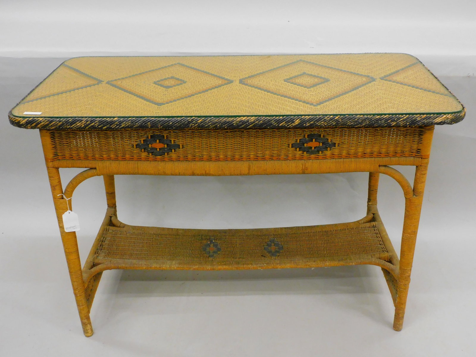 Art Deco wicker table. Circa 1920. Original: polychrome paint with geometric designs. Inset glass top. Original finish. 31" high, 46" long, 23" deep. Shows age appropriate wear and loss to trim paint. Mary Jean McLaughlin collection.