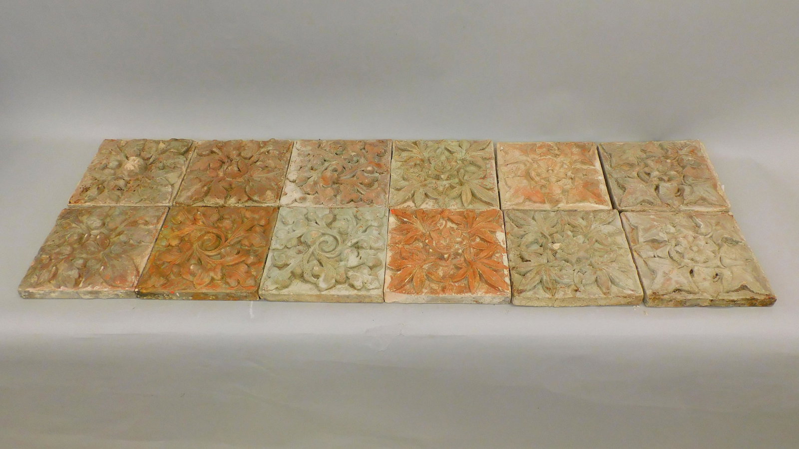 (12) terracotta architectural tiles with floral: and leaf design. Early 20th century. The tiles were salvaged from a building torn down in downtown New Bedford. 9" x 9 1/2" x 1" thick. Minor wear and chipping.