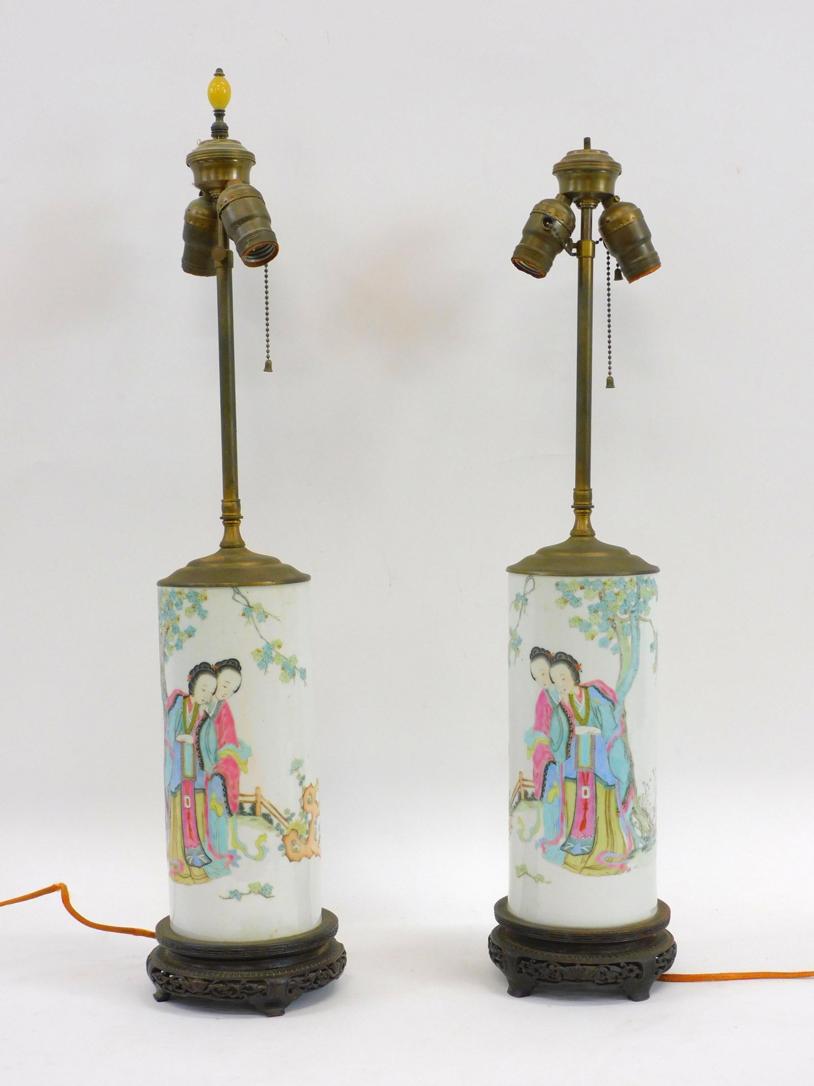 Pair of Chinese porcelain lamps. Scenes depict a: pair of ladies in a garden. They are on a carved wood base. Each lamp measures 28" high by 6 1/2" diameter. One finial missing. Probably needs to be rewired.