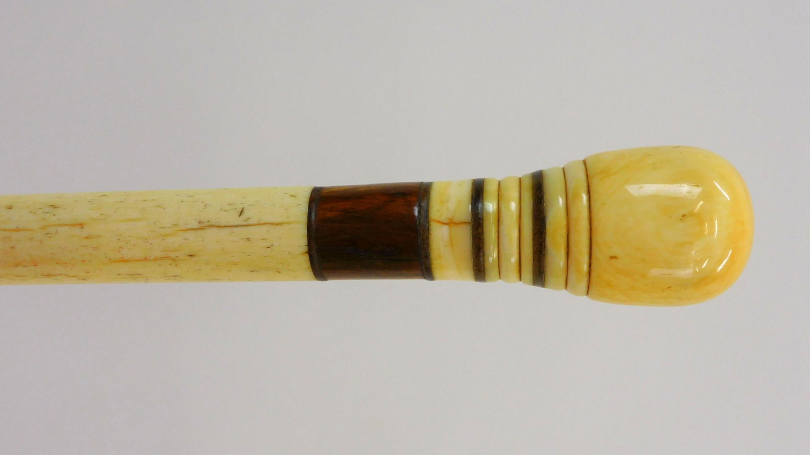 Scrimshaw Walking Stick. 19th century. A turned: whale's tooth knob with green baleen and exotic wood inlay bands, panbone shaft with a steel tip. 34" length. Very good condition. Deaccessioned from the New Bedford Whaling Museum.