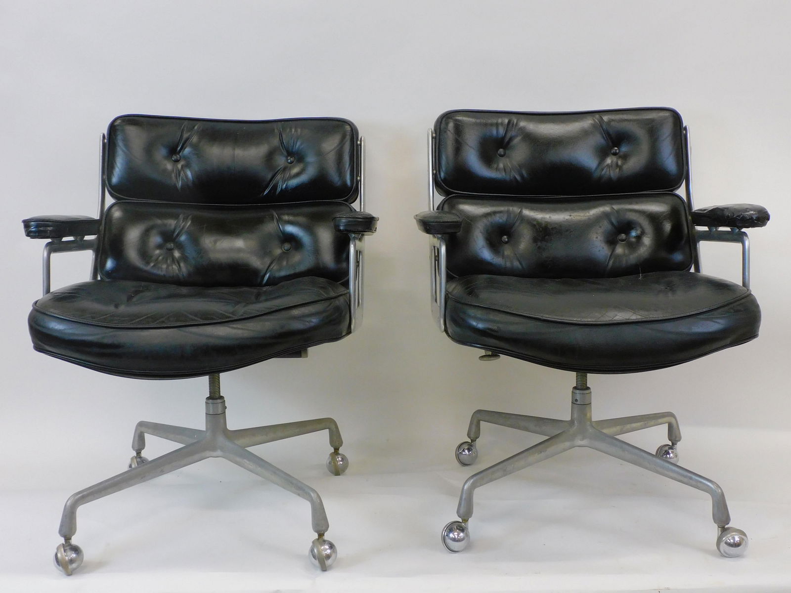 (2) Charles Eames for Herman Miller Time-Life: Executive Chairs. A pair of vintage signed Herman Miller chairs in black leather. Signed on underside. Polished aluminum. Leather. Swiveling office chairs. Shows wear. Worn leather. Shows tape over te